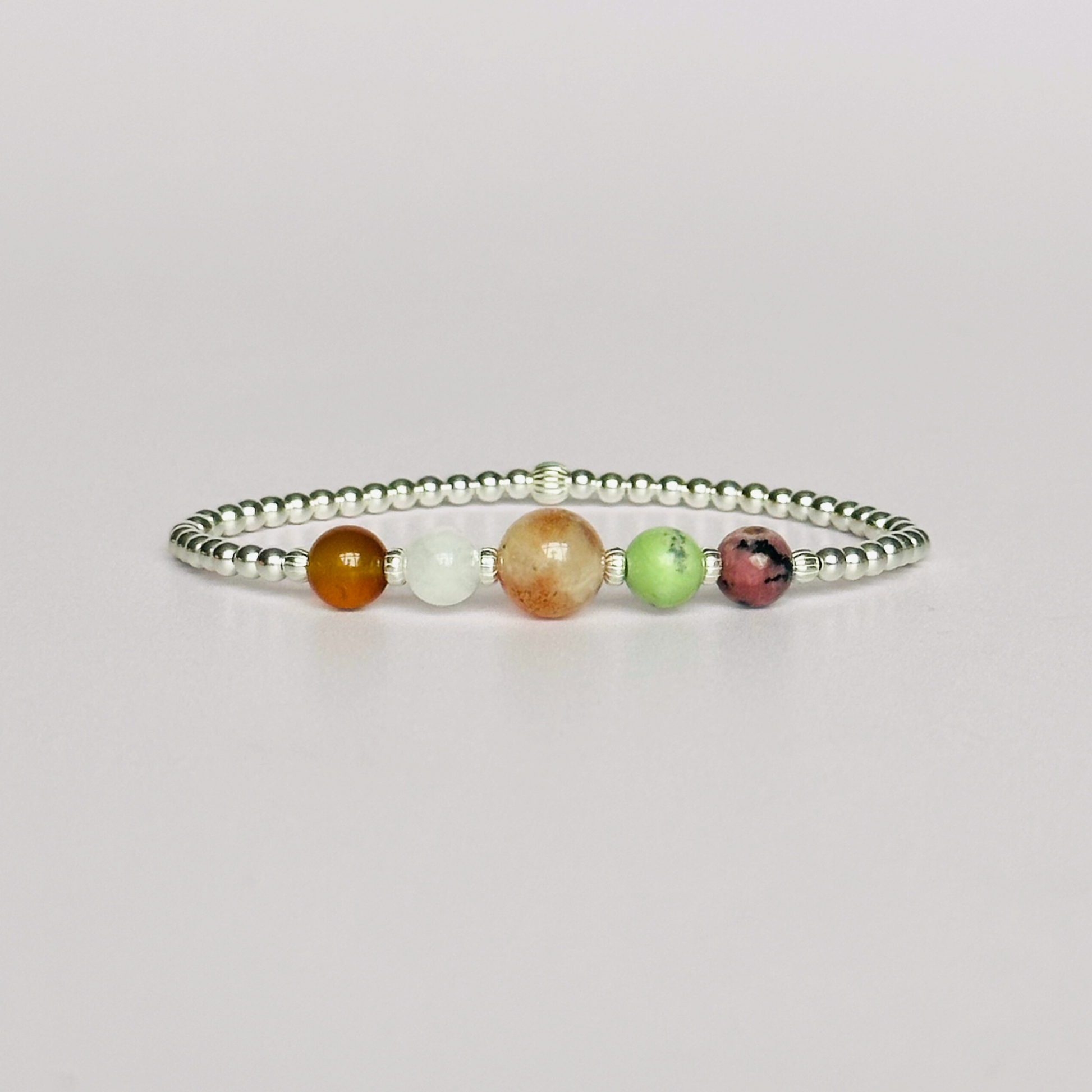 This sterling silver Cancer bracelet is made with a selection of five healing crystals all believed to resonate with the Cancer zodiac sign. The central bead is 8mm, the other four are 6mm. On an elasticated band of 3mm sterling silver beads with corrugated accent beads. Featuring chrysoprase, rhodonite, sunstone, carnelian and moonstone.
