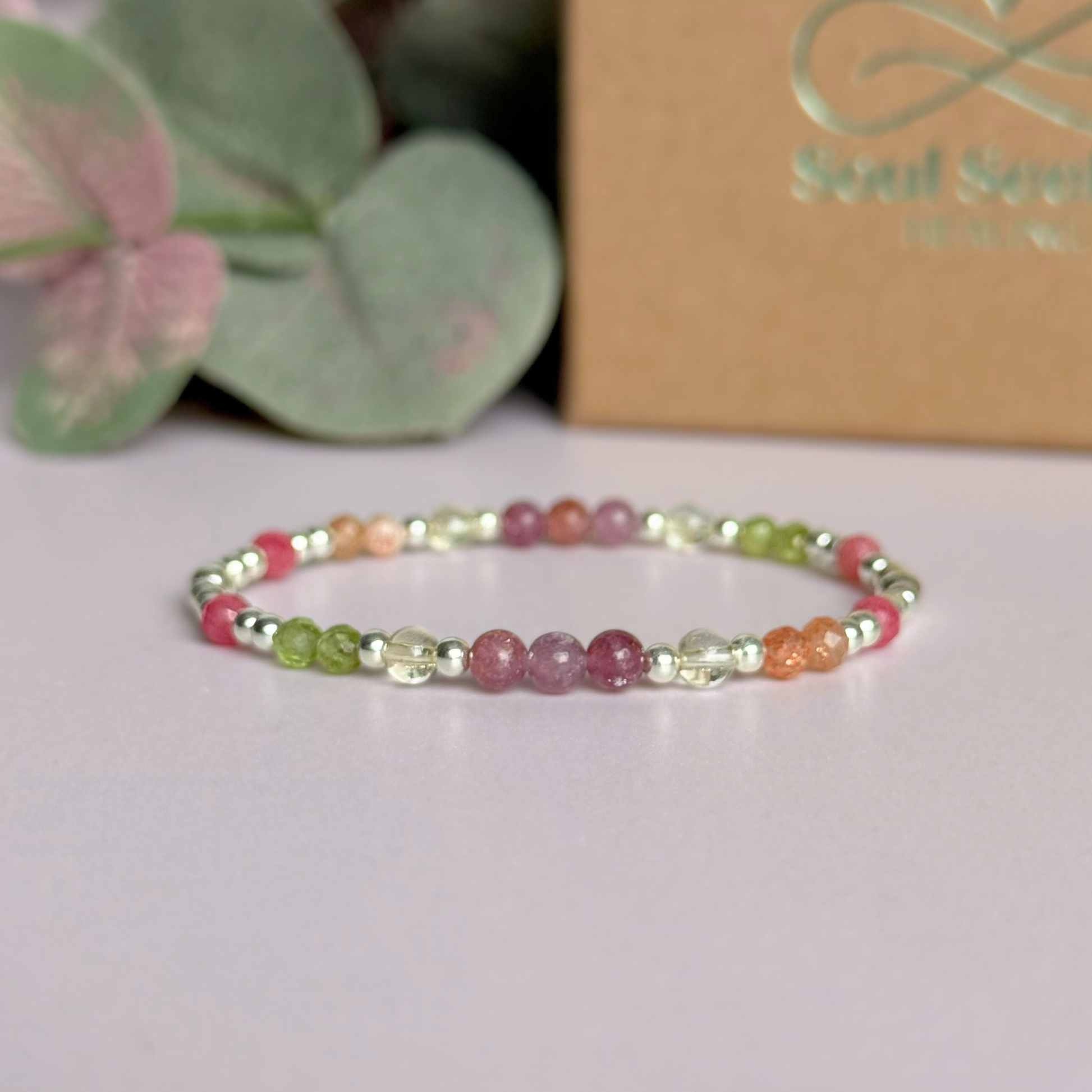 Dainty crystal bracelet featuring a carefully curated selection of genuine crystal beads inspired by wildflowers and free-spirited growth. Featuring 4mm smooth and faceted round gemstone beads with 3mm round accent beads in either sterling silver or gold vermeil. With peridot, sunstone, rhodochrosite, citrine and lepidolite. Picture features the bracelet in silver, with the gift box in the background.