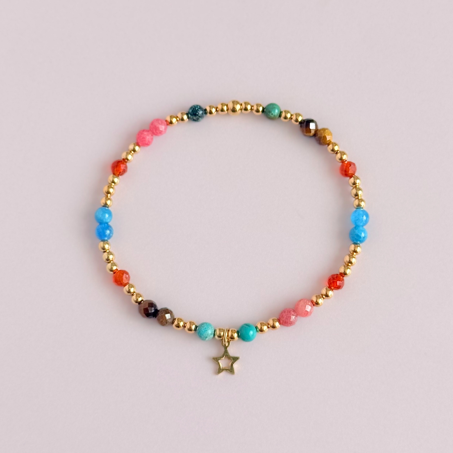 'Hot girl summer' gold vermeil dainty beaded bracelet with tigers eye, turquoise, apatite, carnelian and rhodochrosite. With a beautiful open star charm.Made with round 3mm gold vermeil beads and 4mm smooth and faceted round crystal gemstone beads. Pictured from above, against a pink background.
