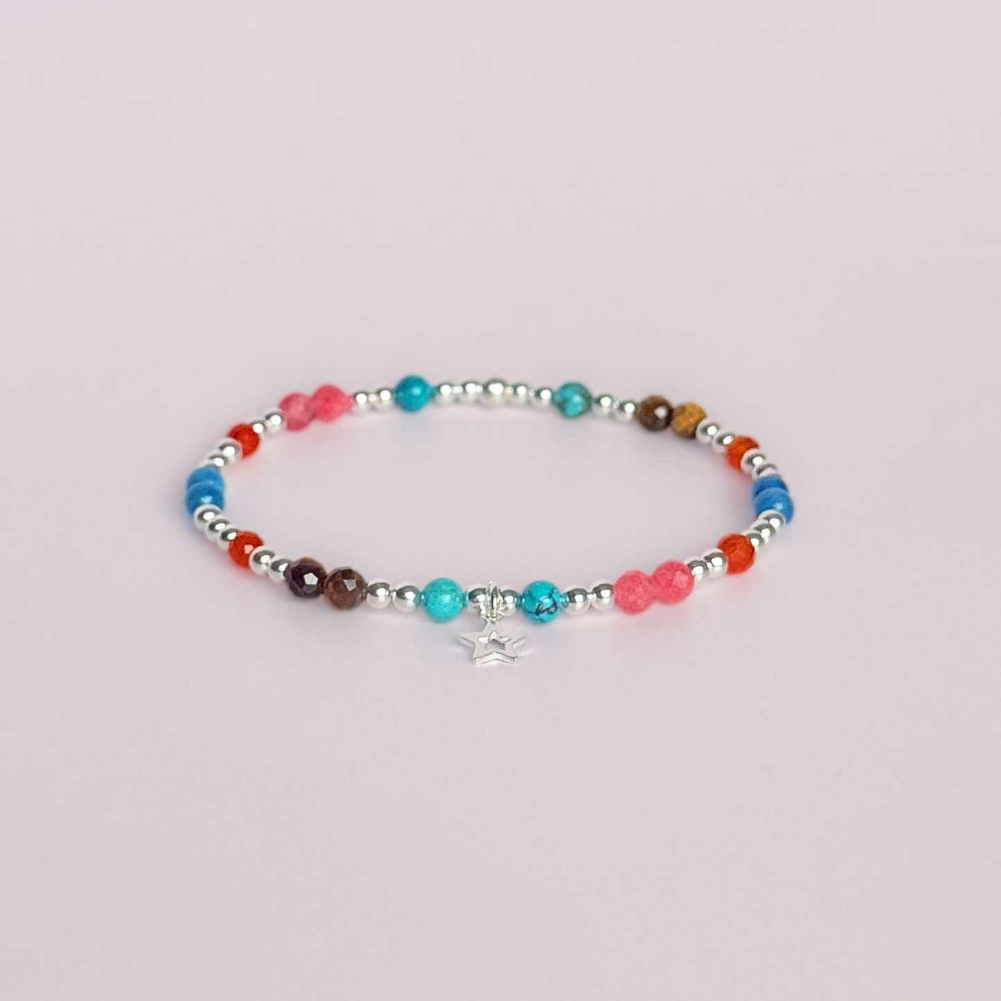 'Hot girl summer' sterling silver dainty beaded bracelet with tigers eye, turquoise, apatite, carnelian and rhodochrosite. With a beautiful open star charm. Made with round 3mm sterling silver beads and 4mm smooth and faceted round crystal gemstone beads. Pictured against a pink background.