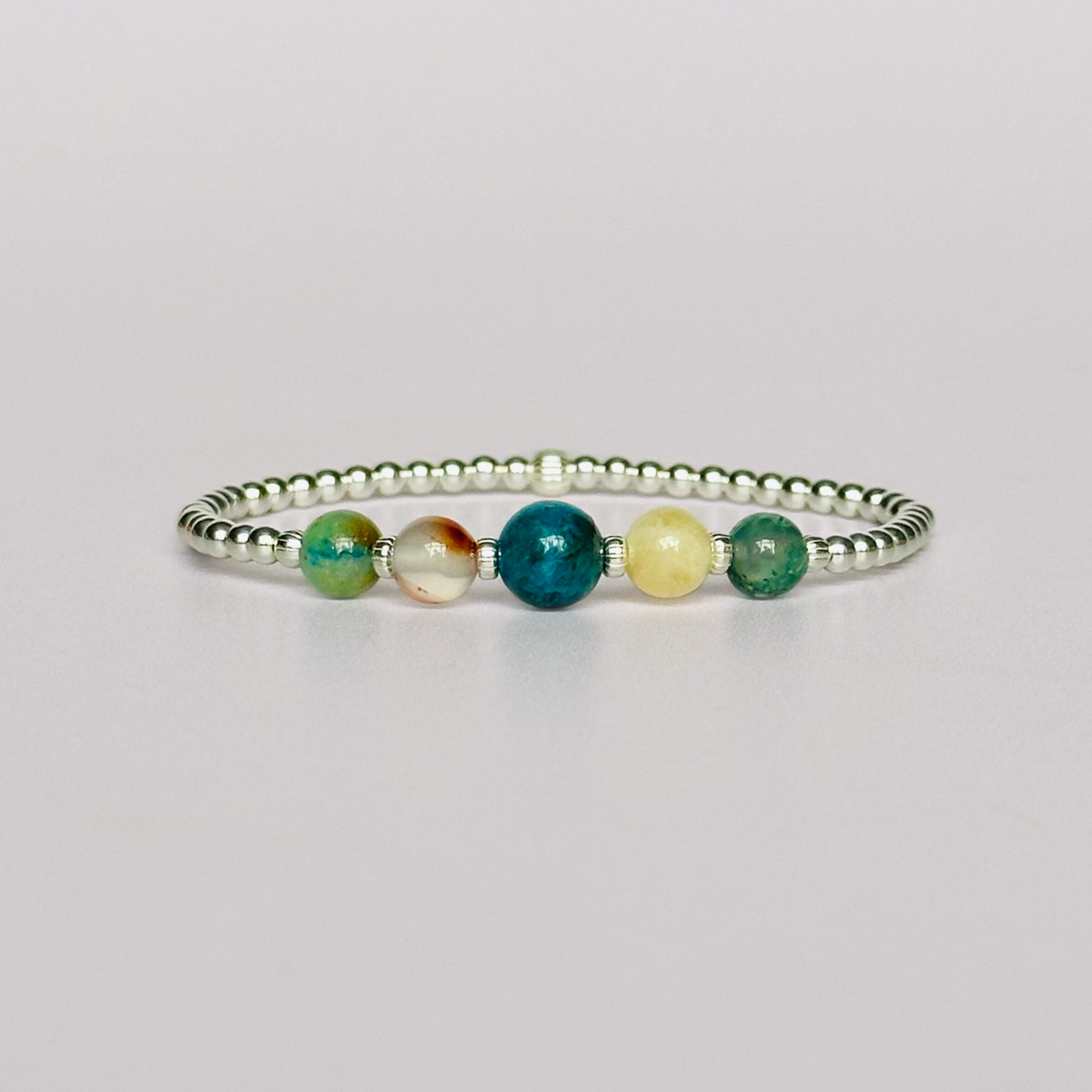 This sterling silver Gemini bracelet is made with a selection of five healing crystals all believed to resonate with the Gemini zodiac sign. The central bead is 8mm, the other four are 6mm. On an elasticated band of 3mm sterling silver beads with corrugated accent beads. Featuring chrysocolla, dendritic agate, apatite, yellow calcite and moss agate.