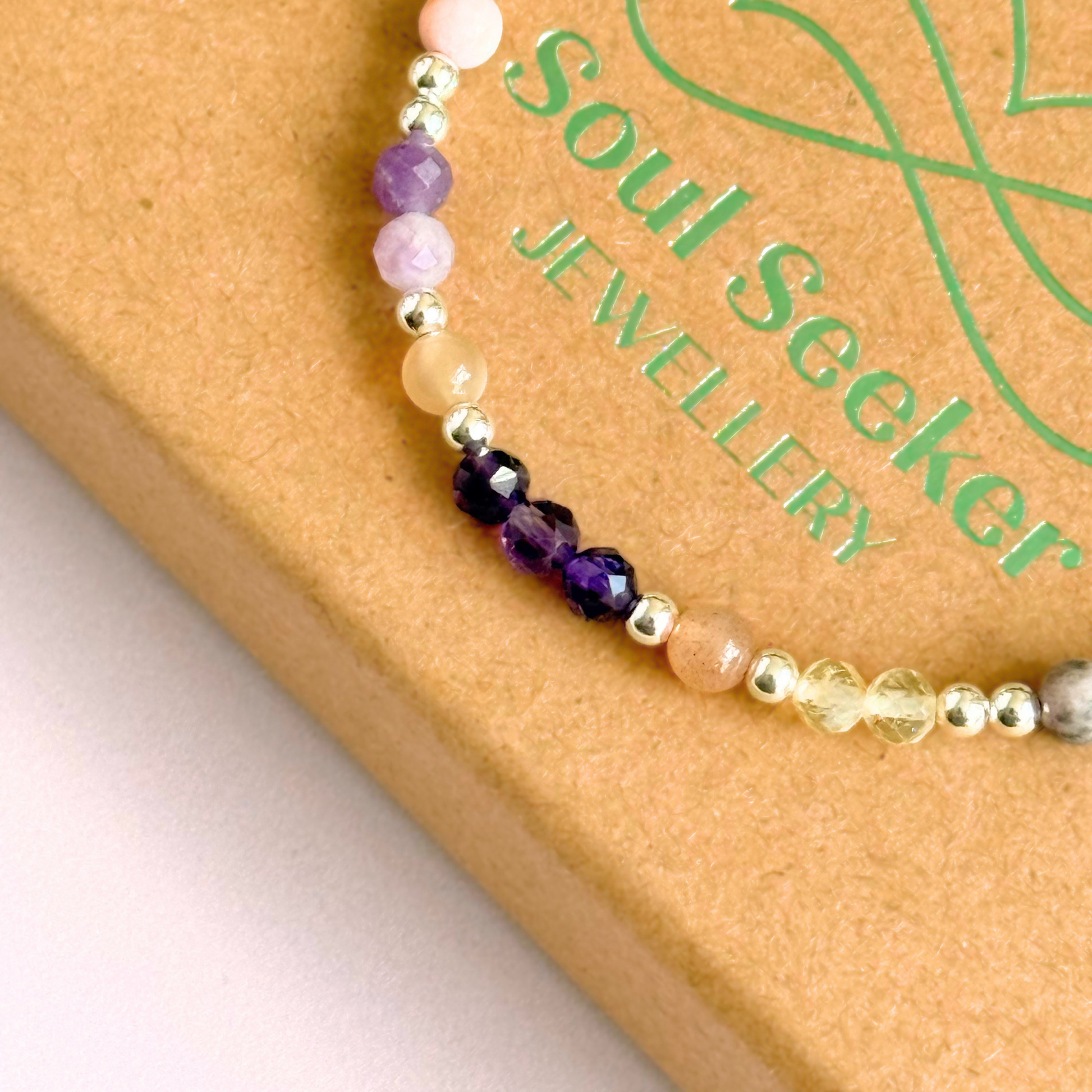 Dainty sterling silver crystal bracelet featuring five crystals, in 4mm faceted and smooth round style, each believed to help with menopause symptoms. Featuring amethyst, citrine, lepidolite, peach moonstone and pink zebra jasper. Close up picture on top of gift box.