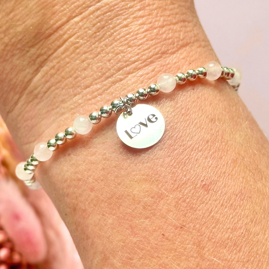 Sterling silver elasticated bracelet featuring 4mm round rose quartz beads, separated by 3mm sterling silver round ball beads. Featuring an 11mm sterling silver round disc charm engraved with the words love. One side of the charm can be personalised if required.