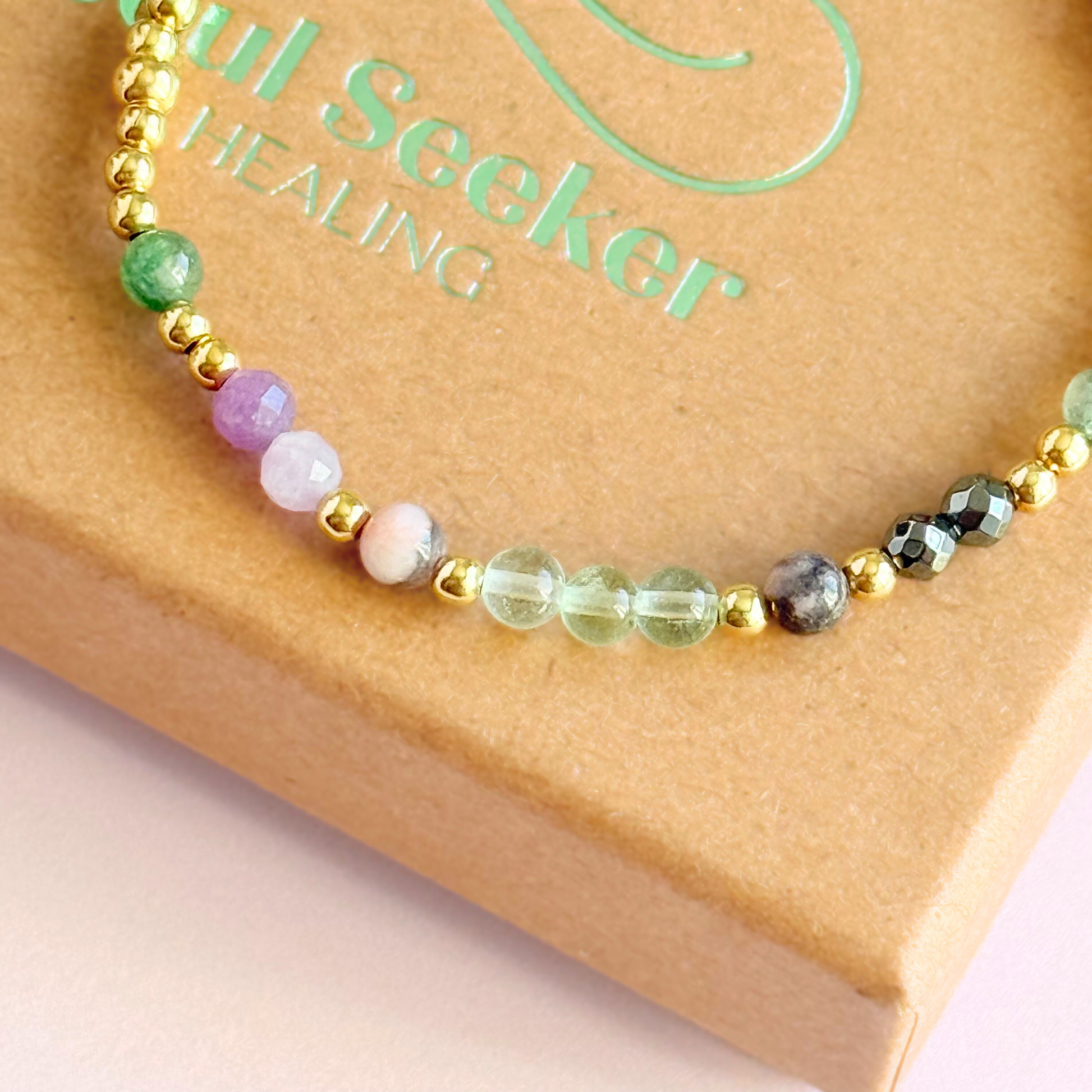 Dainty crystal bracelet featuring five crystals all believed to help with focus, clarity and overwhelm. Featuring fluorite, hematite, lepidolite, moss agate and pink zebra jasper. Featuring 3mm gold vermeil round beads and 4mm faceted round and smooth round crystal beads. Close-up picture of the bracelet on top of the gift box.￼