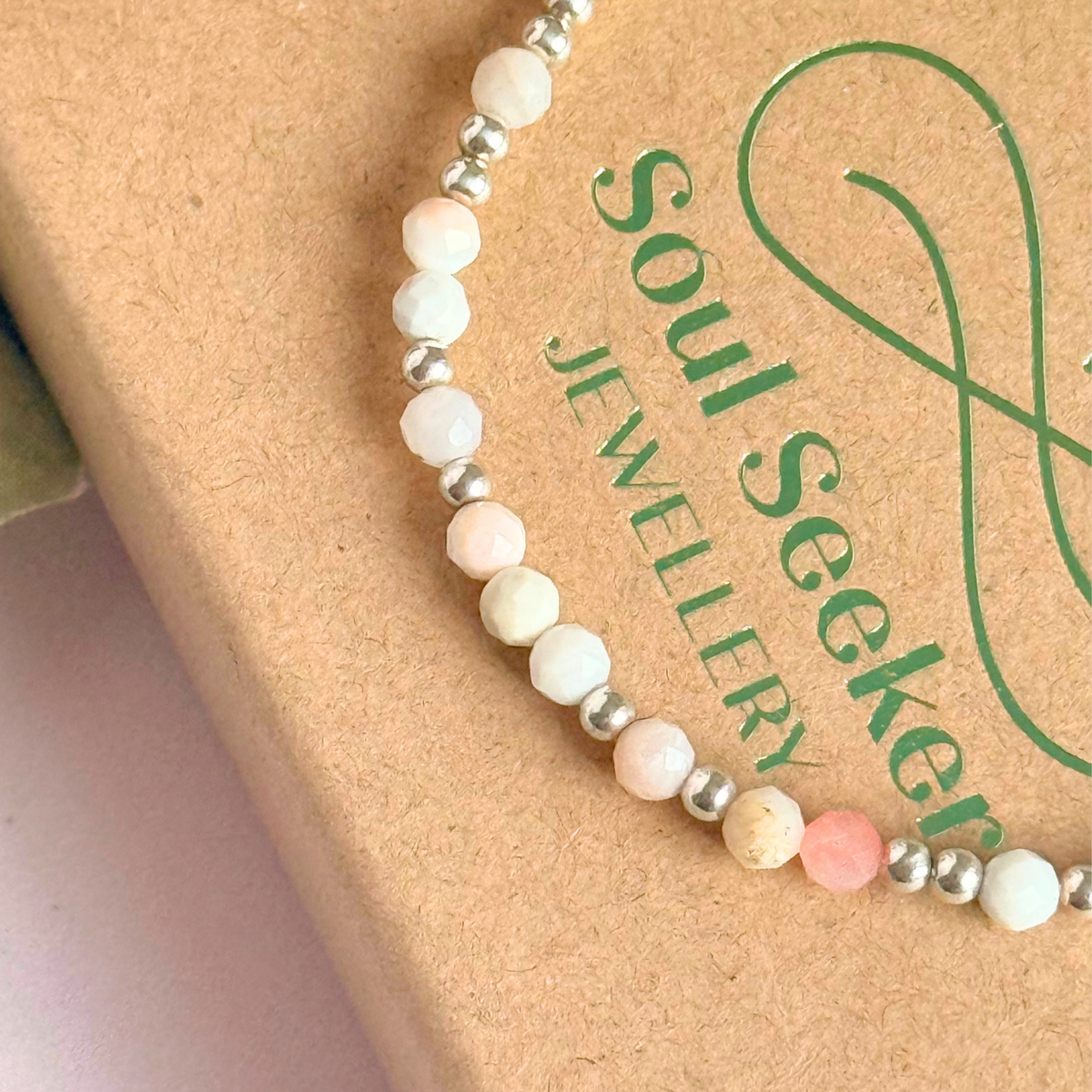 Dainty, minimalist sterling silver and pink opal October birthstone stacking bracelet. Made with 4mm faceted pink opal beads and 3mm sterling silver round beads. Elasticated for comfort. Pictured close up, on top of the gift box