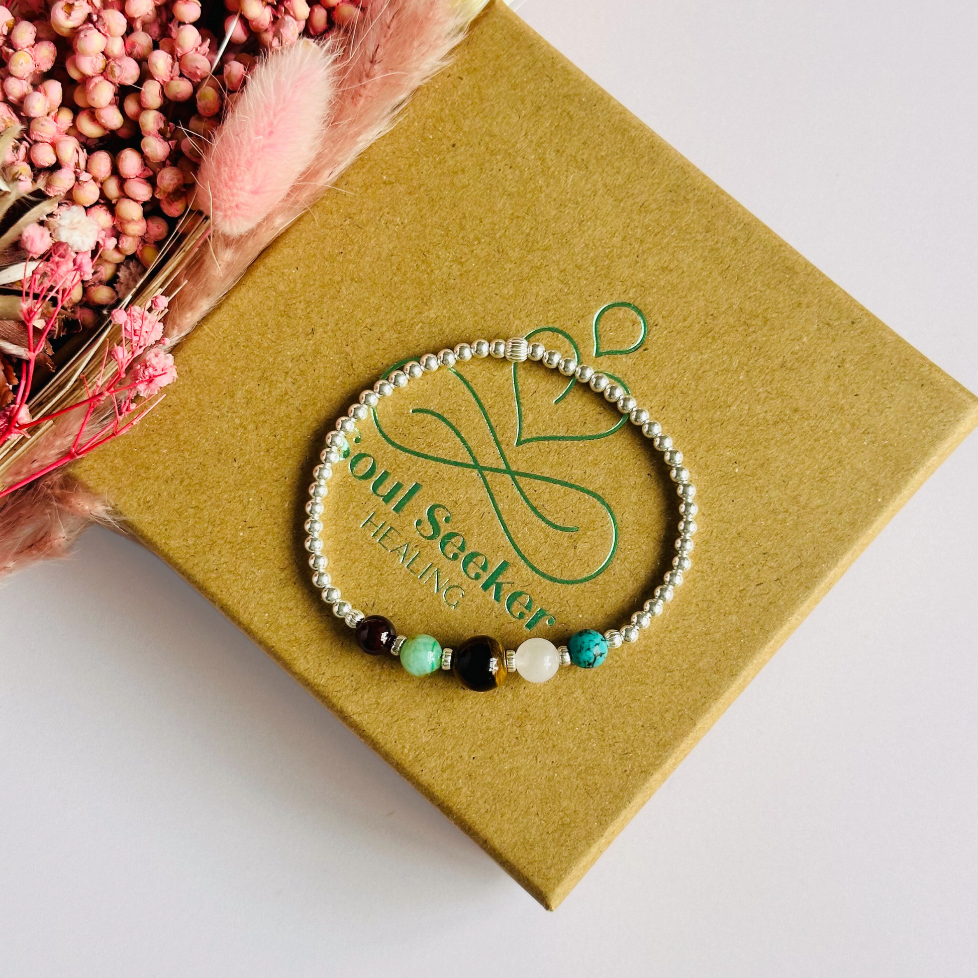 This sterling silver Leo bracelet is made with a selection of five healing crystals all believed to resonate with the Leo zodiac sign. The central bead is 8mm, the other four are 6mm. On an elasticated band of 3mm sterling silver beads with corrugated accent beads. Featuring chrysocolla, garnet, tigers eye, rose quartz and turquoise.