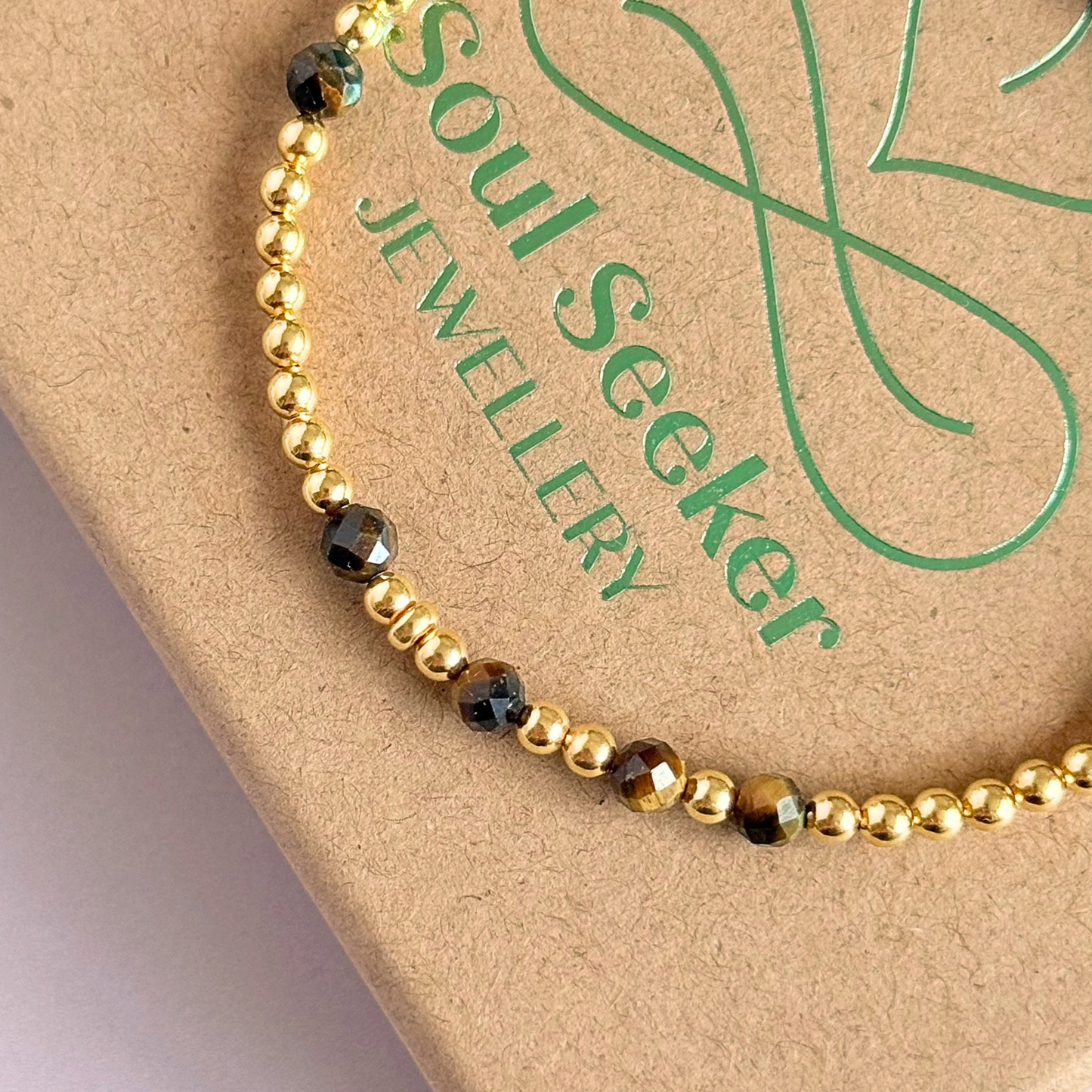 Tigers eye morse code bracelet that spells out the words ‘Ask, believe, receive’ in a combination of 4mm round smooth and faceted crystal beads with your choice of sterling silver or gold vermeil accent beads. Pictured close up, in gold on the box
