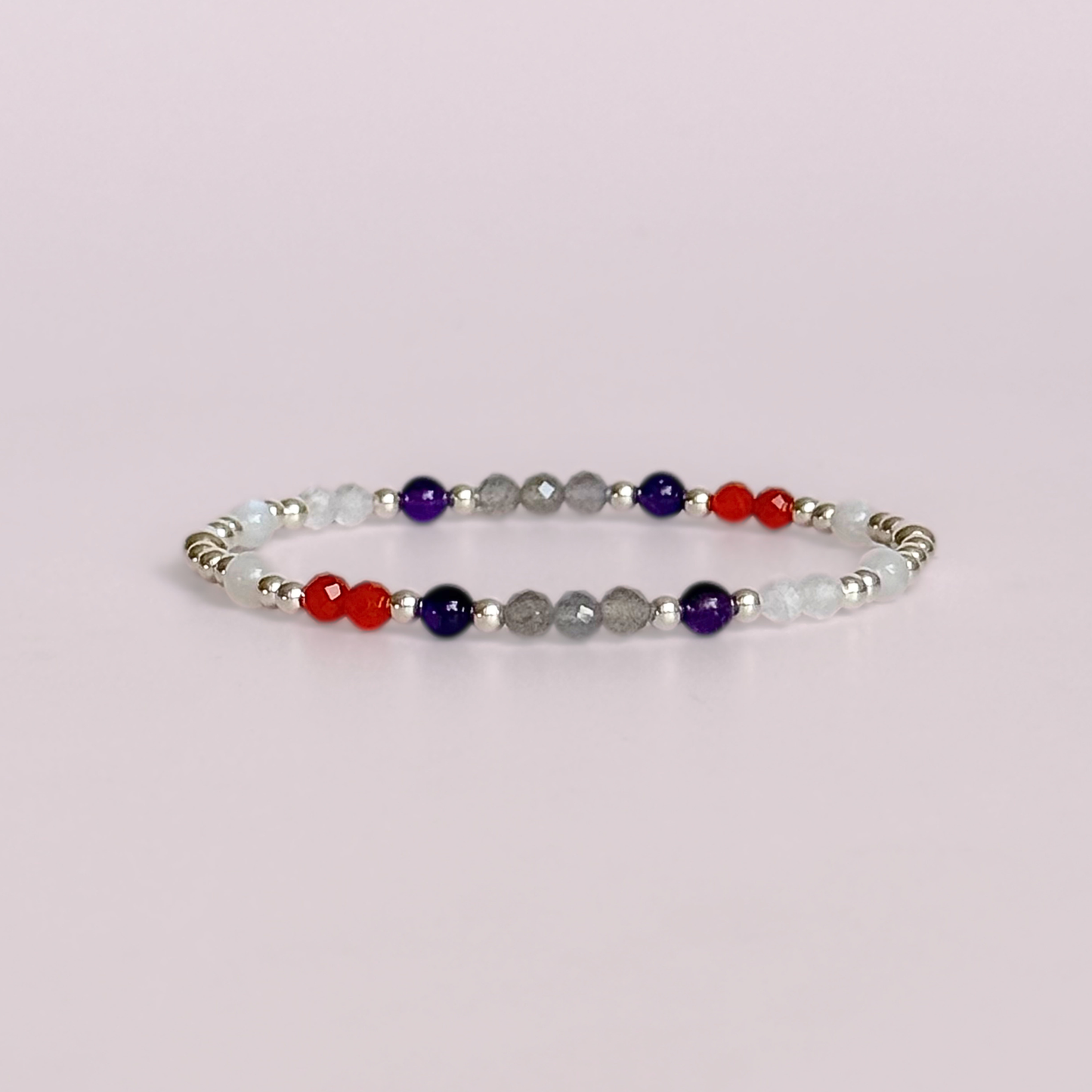 Dainty sterling silver crystal bracelet featuring five crystals, in 4mm faceted and smooth round style, each believed to help with hormonal balance. Featuring amethyst, moonstone, carnelian, labradorite and rose quartz. Pictured against a light pink background.