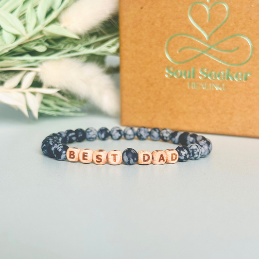 Men’s crystal bracelet with 6mm frosted snowflake obsidian gemstone crystal beads and laser engraved wooden letter beads featuring the word best dad or can also be made with any other words or letters.
