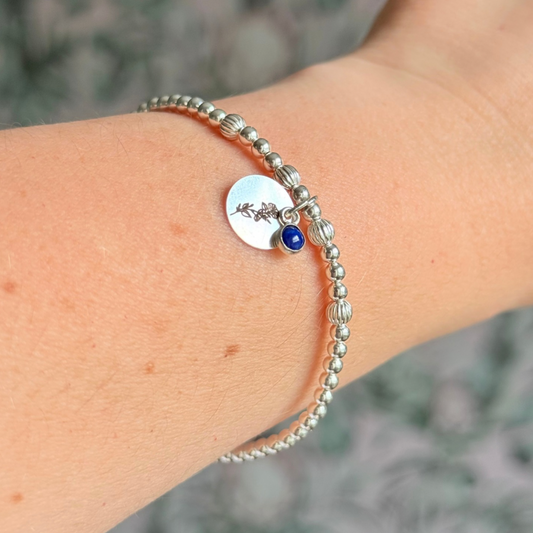 This sterling silver bracelet features a domed 4mm lapis lazuli cabochon charm, the birth stone for September, in a sterling silver setting. It features an 11mm sterling silver disc charm, which is engraved with the September birth flower, Morning Glory. This charm can be personalised on one side if required or feature the same flower graphic on both sides.  The main band of the bracelet is made up of 3 mm sterling silver round ball beads with some corrugated accent beads.