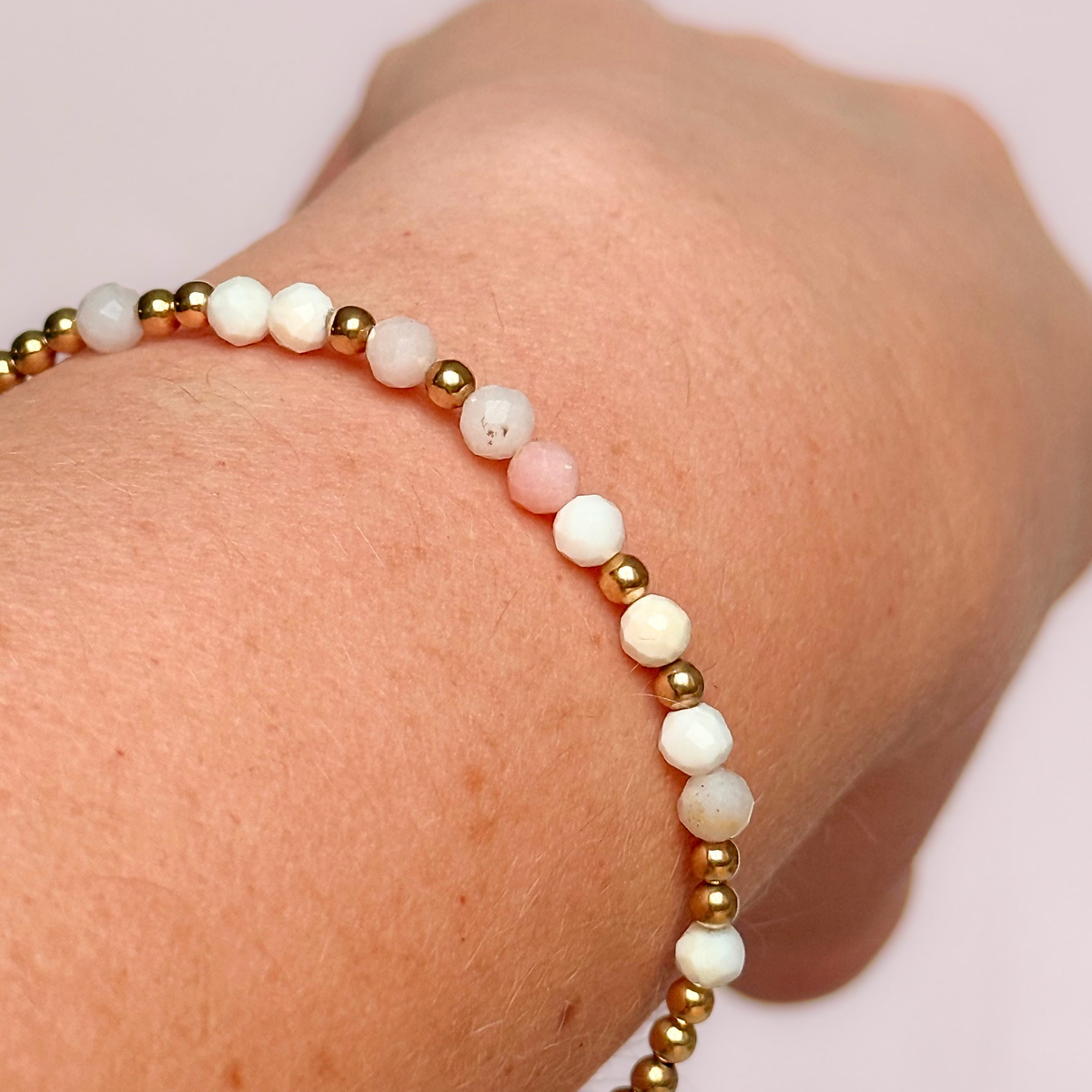 Dainty, minimalist gold vermeil and pink opal October birthstone stacking bracelet. Made with 4mm faceted pink opal beads and 3mm gold vermeil round beads. Elasticated for comfort. Pictured being worn, close up