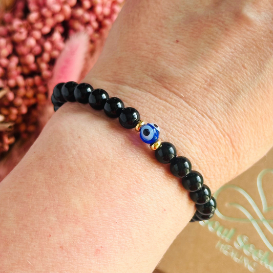 Natural black tourmaline bracelet featuring ethically mined smooth 6mm round beads with a beautiful blue Turkish evil eye glass bead as the focal point. Finished with gold vermeil or sterling silver accent beads.