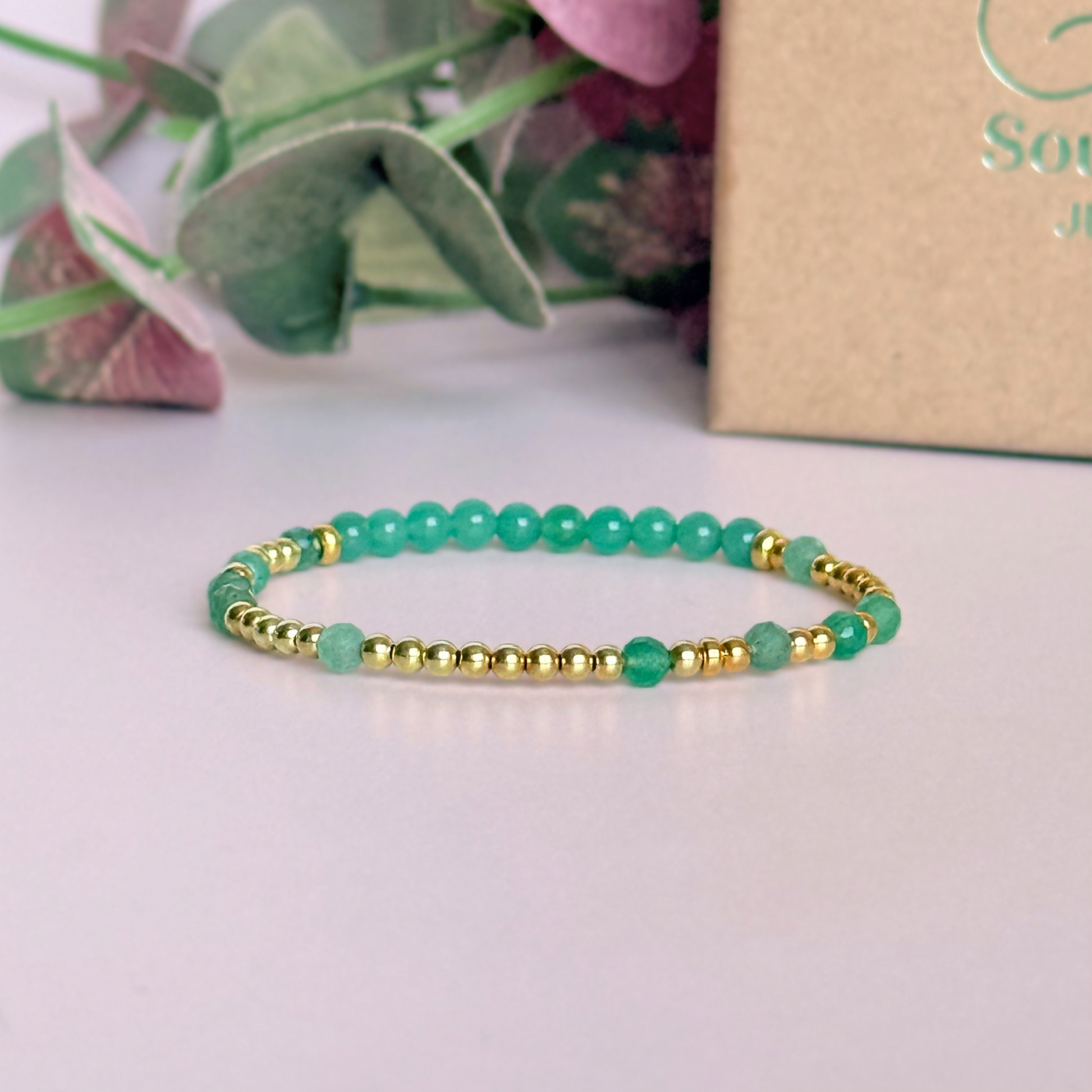 Green aventurine morse code bracelet that spells out the words ‘Ask, believe, receive’ in a combination of 4mm round smooth and faceted crystal beads with your choice of sterling silver or gold vermeil accent beads. Pictured in gold, in front of the gift box