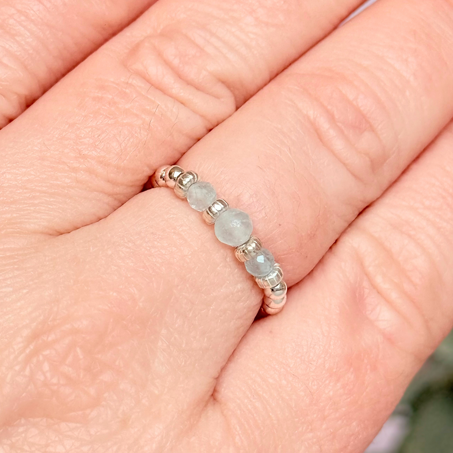 Aquamarine crystal trilogy sterling silver elasticated ring featuring three March birthstone gemstone faceted beads, on a band of sterling silver round beads. The crystals are seperated by sterling silver corrugated rondelles. The main crystal is 4mm and the ones at either side are 3mm. Pictured being worn.