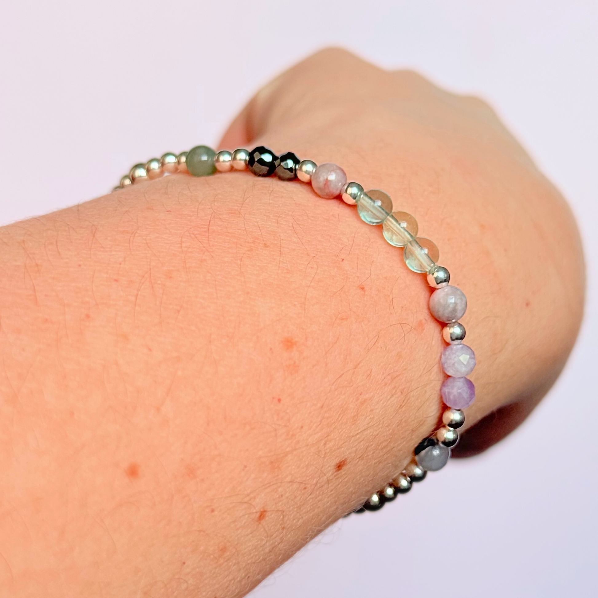Dainty crystal bracelet featuring five crystals all believed to help with focus, clarity and overwhelm. Featuring fluorite, hematite, lepidolite, moss agate and pink zebra jasper. Featuring 3mm sterling silver round beads and 4mm faceted round and smooth round crystal beads. Picture shows the bracelet being worn, on an angle.