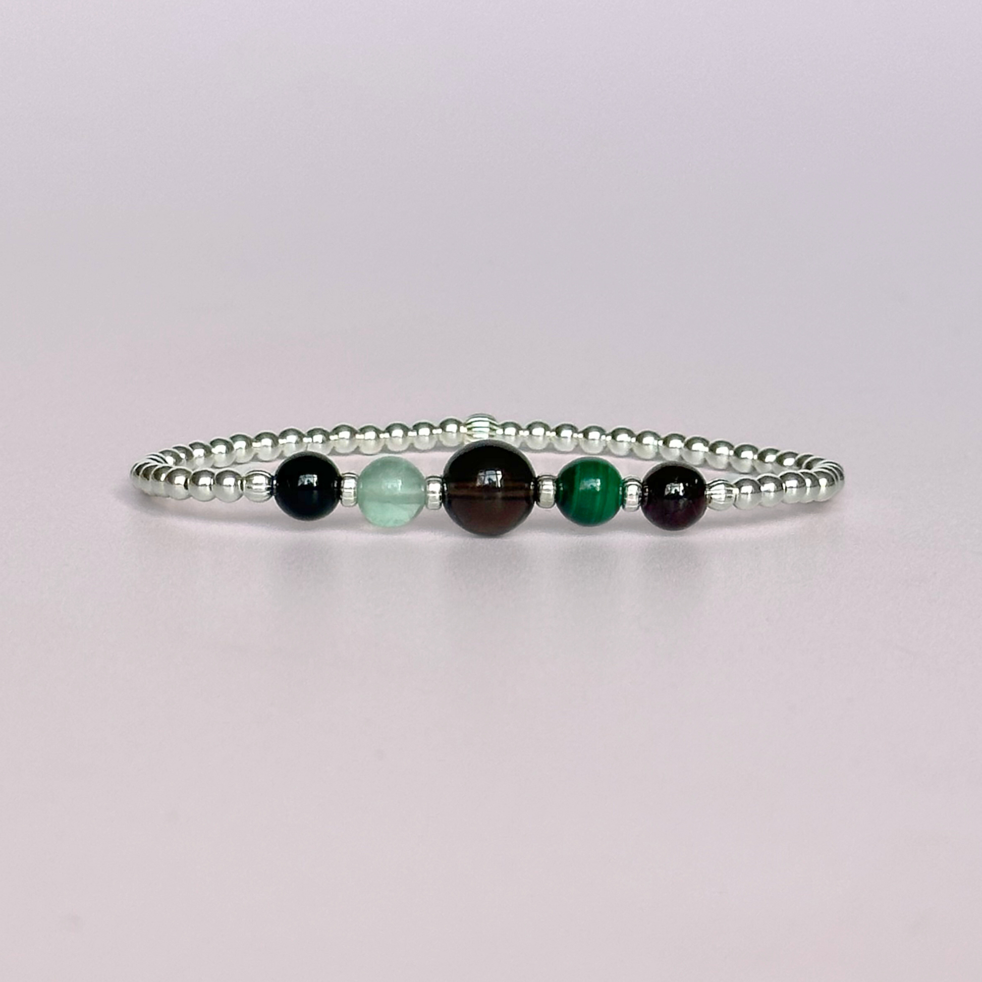 This sterling silver Capricorn bracelet is made with a selection of five healing crystals all believed to resonate with the Capricorn zodiac sign. The central bead is 8mm, the other four are 6mm. On an elasticated band of 3mm sterling silver beads with corrugated accent beads. Featuring garnet, malachite, fluorite, smoky quartz and black tourmaline.
