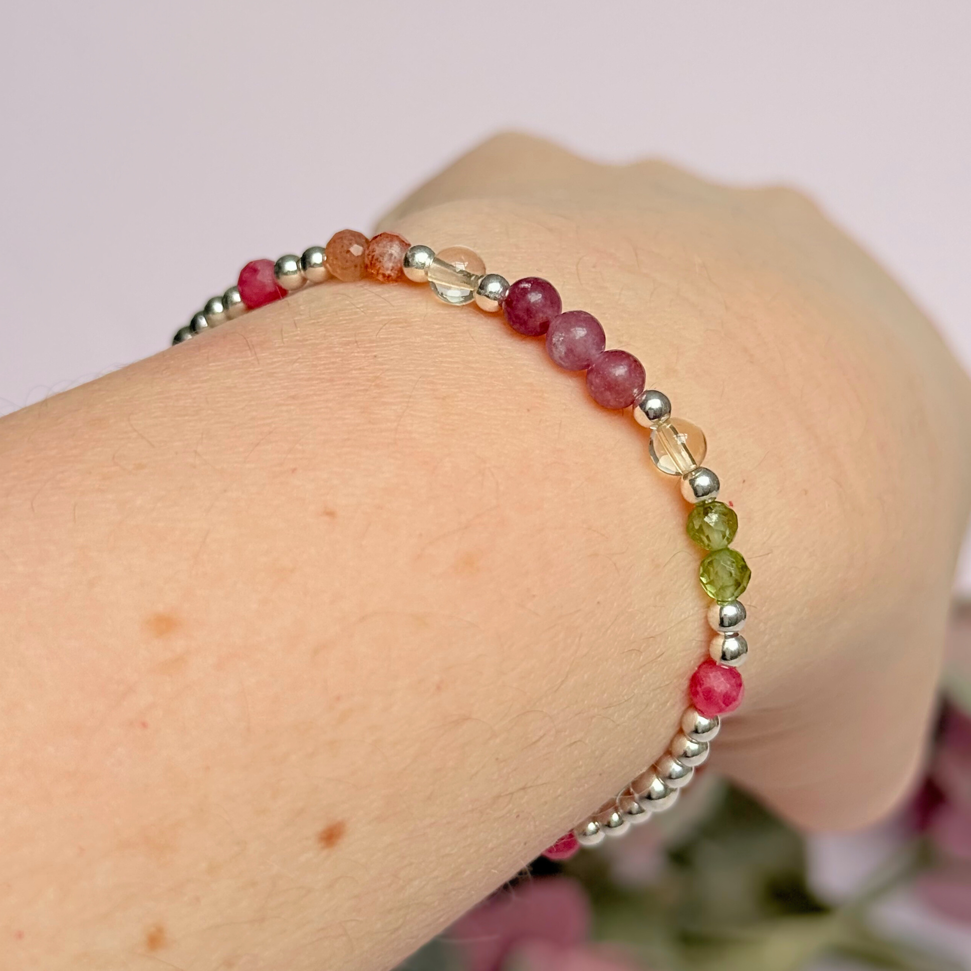 Dainty crystal bracelet featuring a carefully curated selection of genuine crystal beads inspired by wildflowers and free-spirited growth. Featuring 4mm smooth and faceted round gemstone beads with 3mm round accent beads in either sterling silver or gold vermeil. With peridot, sunstone, rhodochrosite, citrine and lepidolite. Pictured in silver, shown being worn, at an angle.