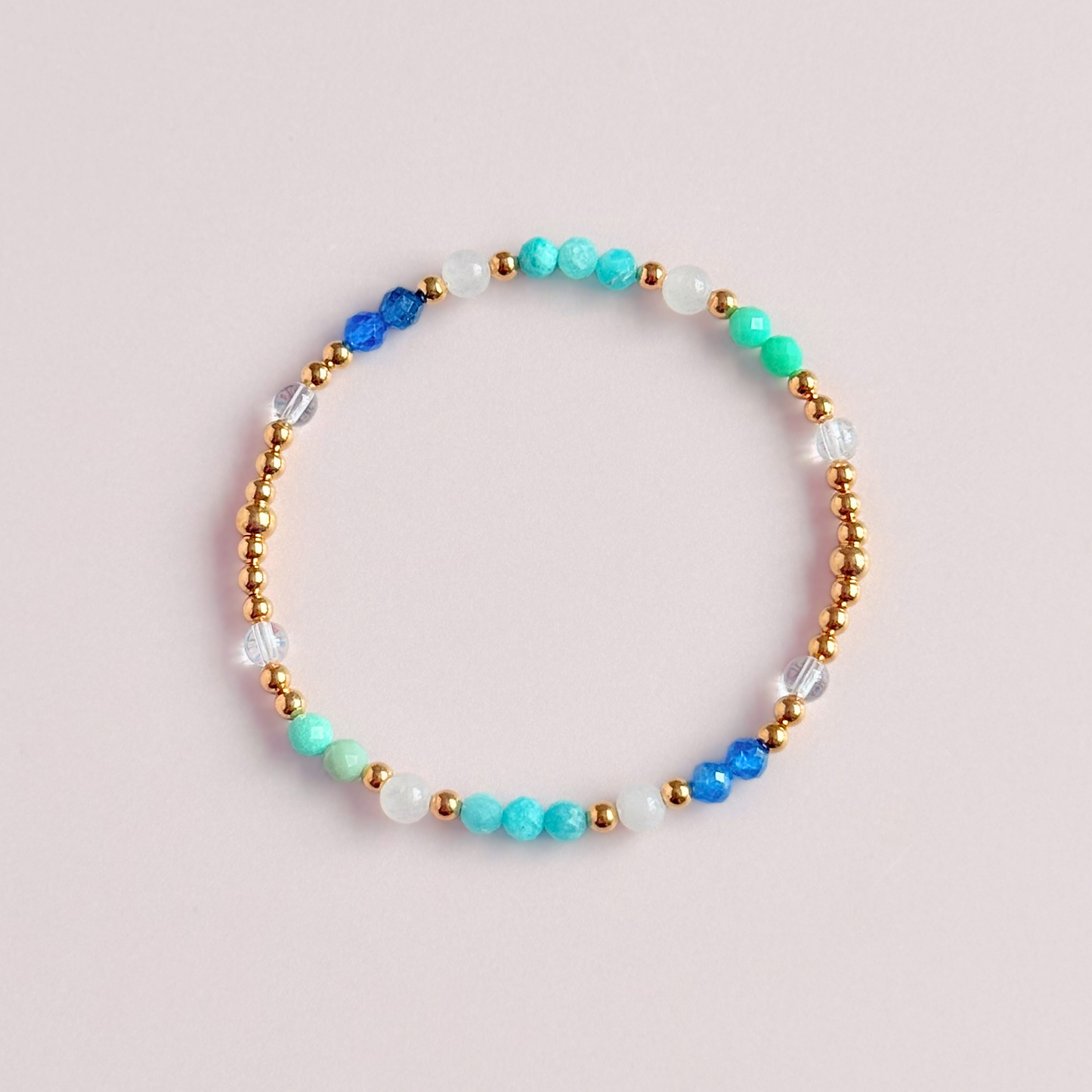 ‘Caribbean Dream' gold vermeil dainty beaded bracelet with white jade, chrysoprase, amazonite, apatite and clear quartz. Made with round 3mm gold vermeil beads and 4mm smooth and faceted round crystal gemstone beads. Pictured from above, against a pink background 