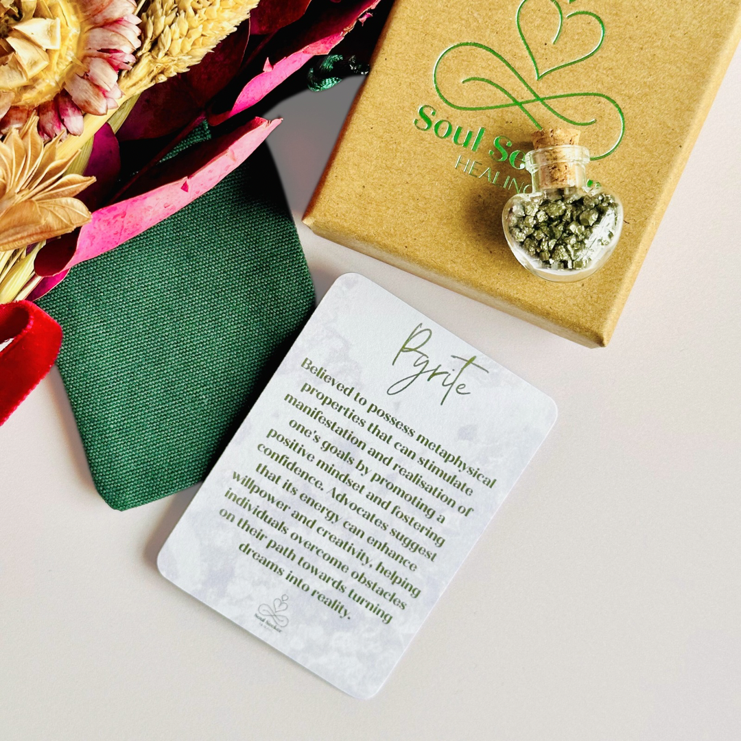 A pretty heart shaped mini glass bottle filled with powerful, ethically mined pyrite crystal chips, presented on an eco-friendly textured card with the words 'Manifest your dreams into reality.’