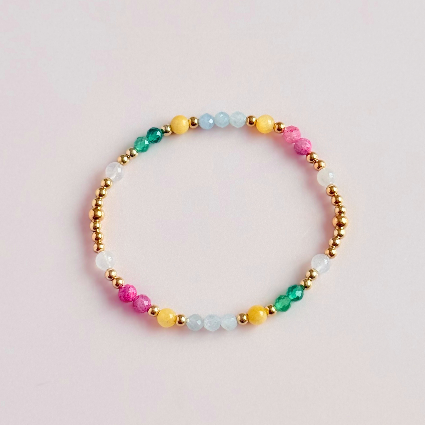 'Amalfi Coast' gold vermeil dainty beaded bracelet with green agate, yellow calcite, pink tourmaline, aquamarine and moonstone. Made with round 3mm gold vermeil beads and 4mm smooth and faceted round crystal gemstone beads. Pictured from above, on a pink background