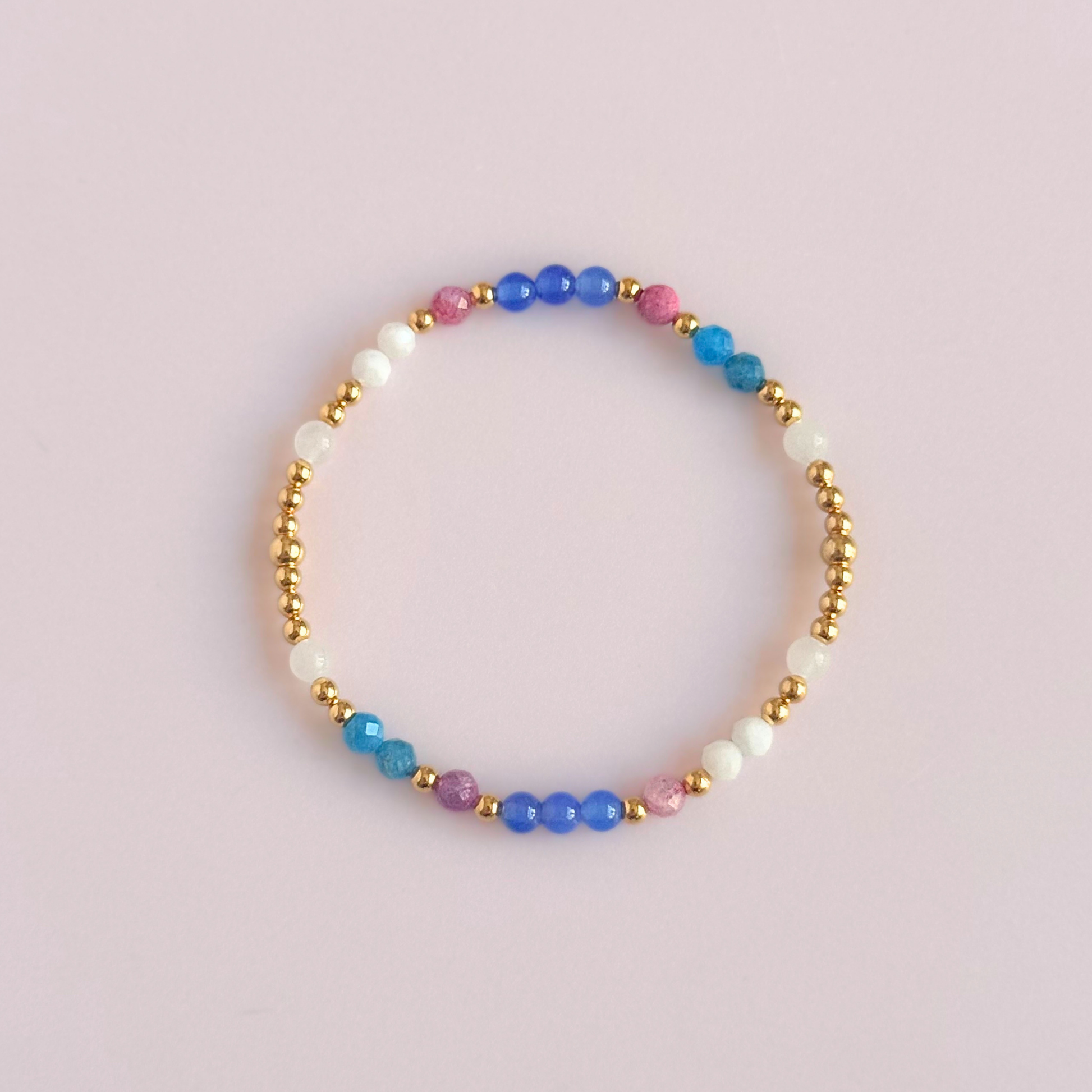 ‘Santorini' gold vermeil dainty beaded bracelet with pink tourmaline, rainbow moonstone, blue agate, apatite and white jade. Made with round 3mm gold vermeil beads and 4mm smooth and faceted round crystal gemstone beads. Pictured from above, against a pink background