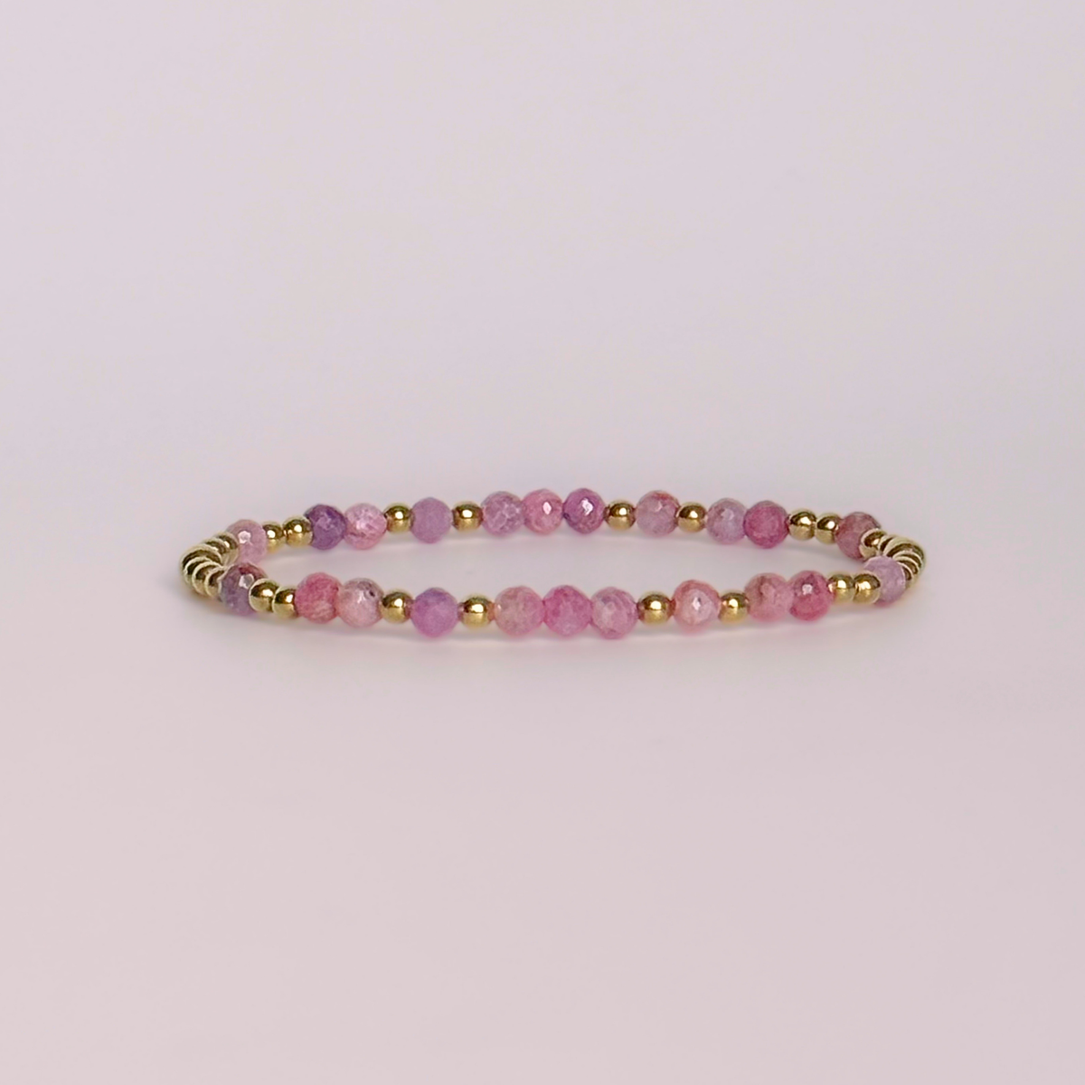 Dainty, minimalist gold vermeil and pink tourmaline October birthstone stacking bracelet. Made with 4mm faceted pink tourmaline beads and 3mm gold vermeil round beads. Elasticated for comfort. Pictured against a light pink background