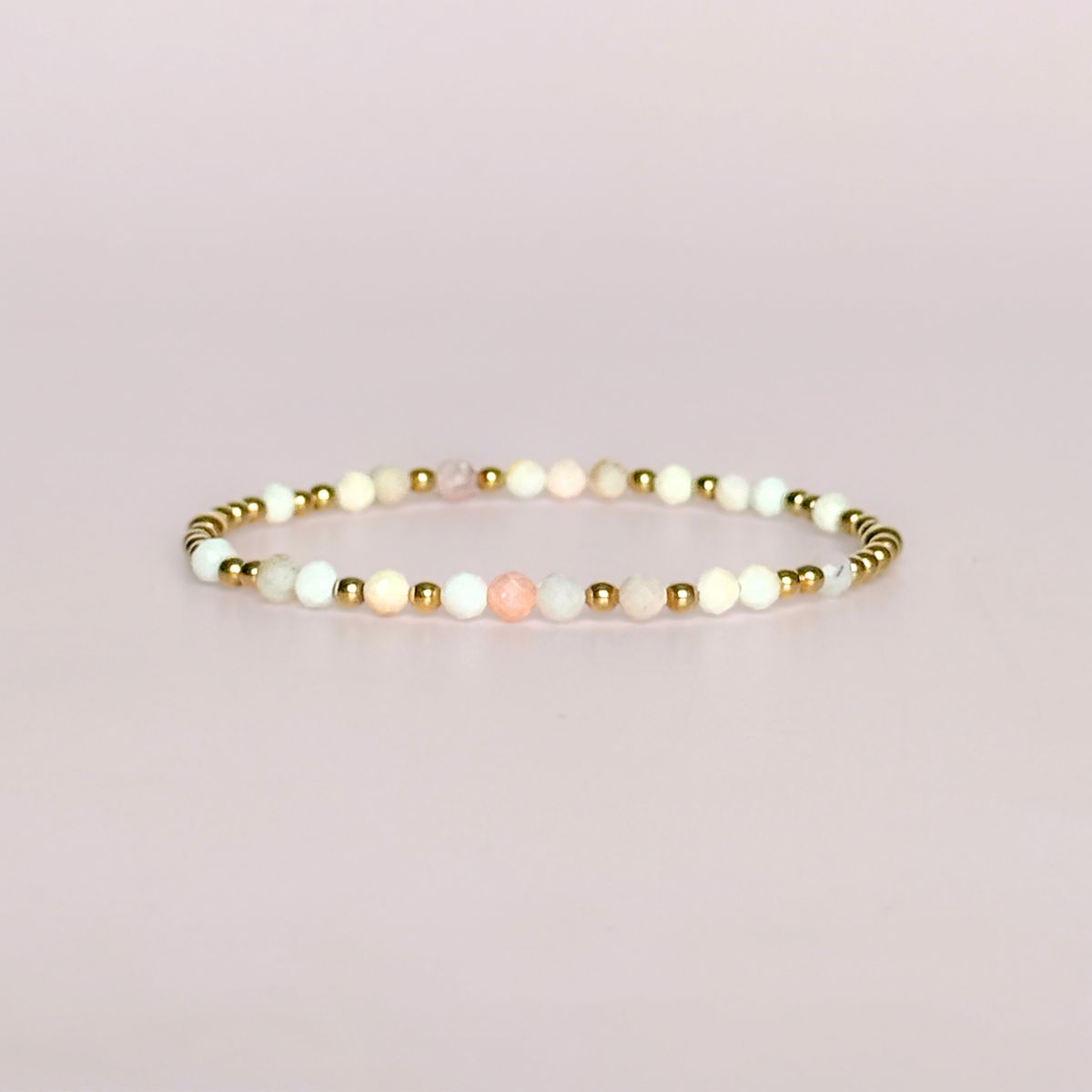 Dainty, minimalist gold vermeil and pink opal October birthstone stacking bracelet. Made with 4mm faceted pink opal beads and 3mm gold vermeil round beads. Elasticated for comfort. Pictured against a light pink background