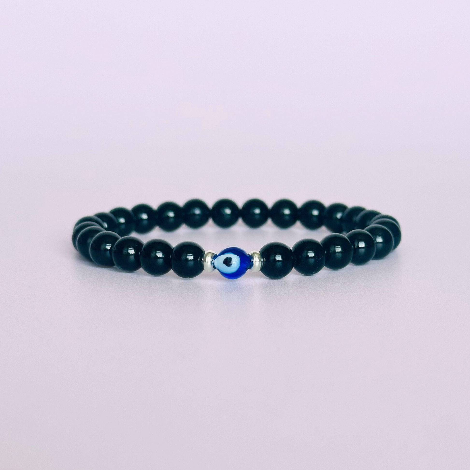 Natural black tourmaline bracelet featuring ethically mined smooth 6mm round beads with a beautiful blue Turkish evil eye glass bead as the focal point. Finished with gold vermeil or sterling silver accent beads.