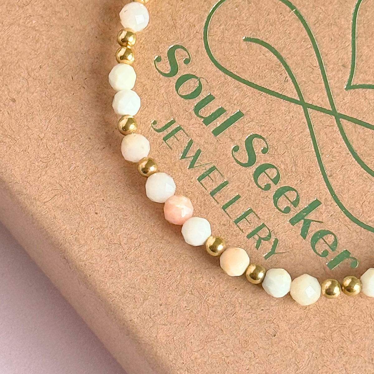 Dainty, minimalist gold vermeil and pink opal October birthstone stacking bracelet. Made with 4mm faceted pink opal beads and 3mm gold vermeil round beads. Elasticated for comfort. Pictured close up, on top of the gift box
