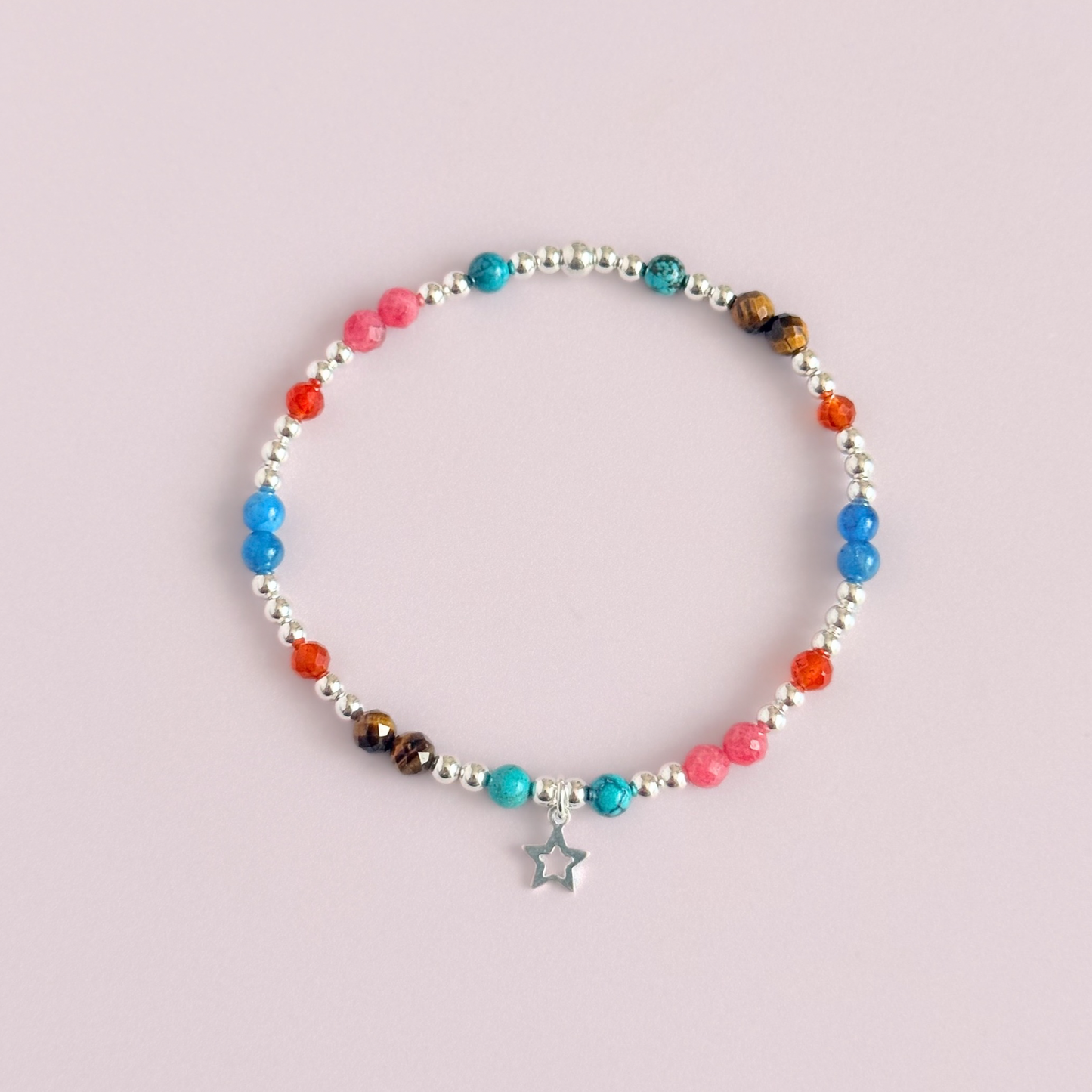 'Hot girl summer' sterling silver dainty beaded bracelet with tigers eye, turquoise, apatite, carnelian and rhodochrosite. With a beautiful open star charm. Made with round 3mm sterling silver beads and 4mm smooth and faceted round crystal gemstone beads. Pictured from above, against a pink background.