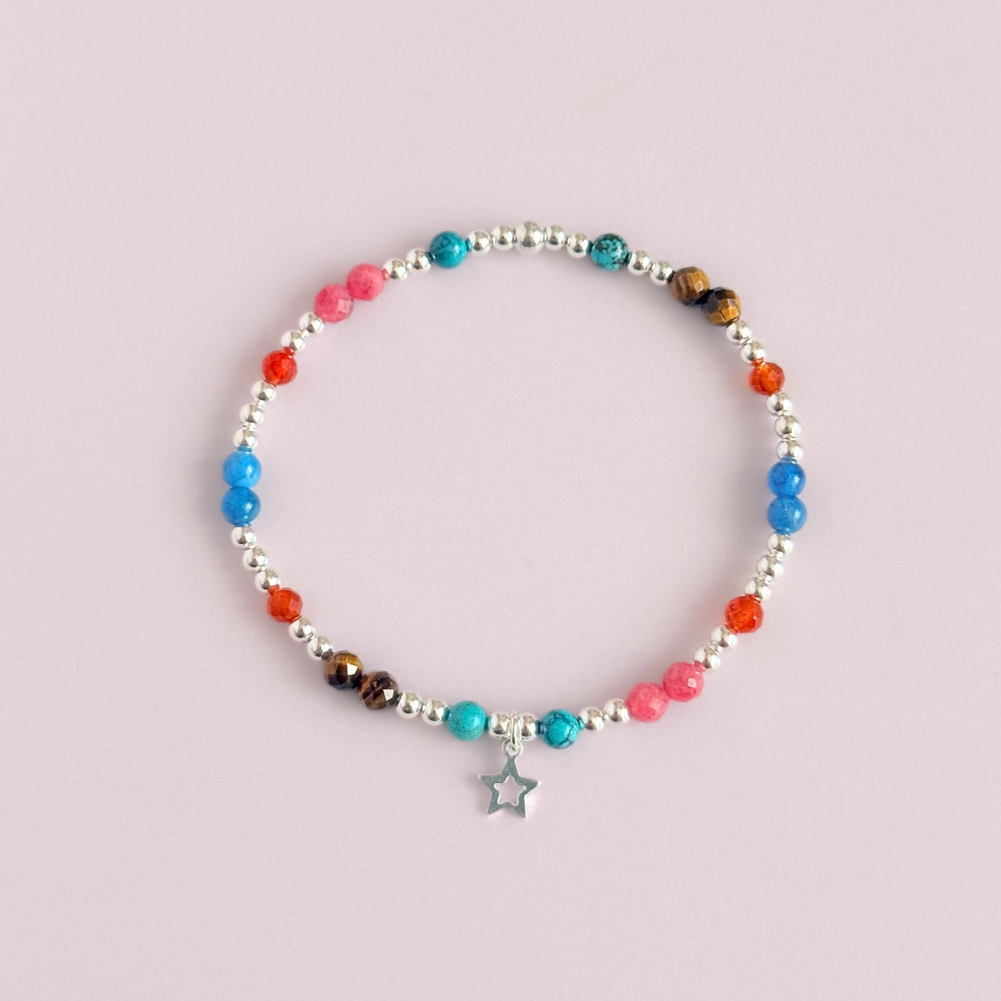 'Hot girl summer' sterling silver dainty beaded bracelet with tigers eye, turquoise, apatite, carnelian and rhodochrosite. With a beautiful open star charm. Made with round 3mm sterling silver beads and 4mm smooth and faceted round crystal gemstone beads. Pictured from above, against a pink background.