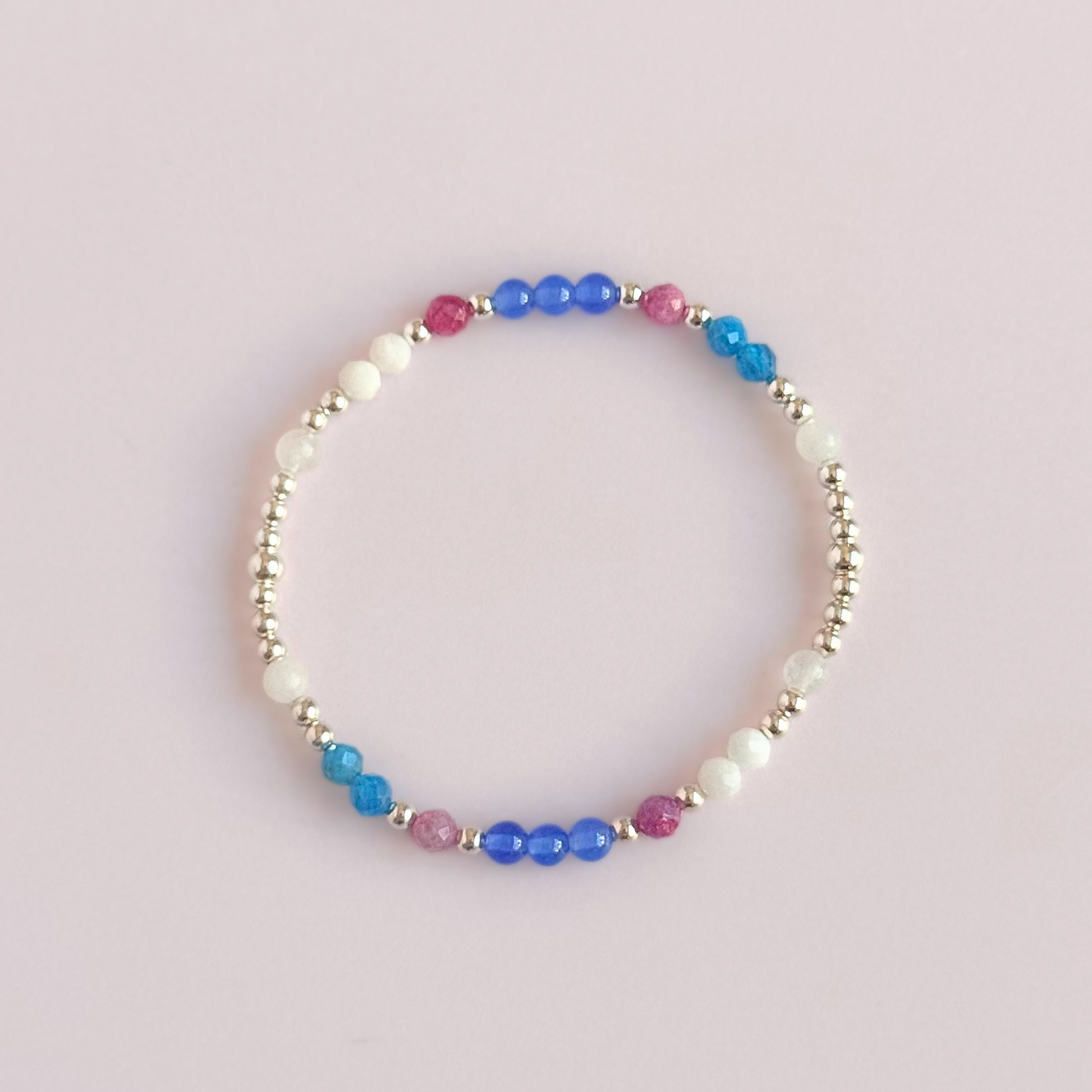 ‘Santorini' sterling silver dainty beaded bracelet with pink tourmaline, rainbow moonstone, blue agate, apatite and white jade. Made with round 3mm sterling silver beads and 4mm smooth and faceted round crystal gemstone beads. Pictured from above, against a pink background