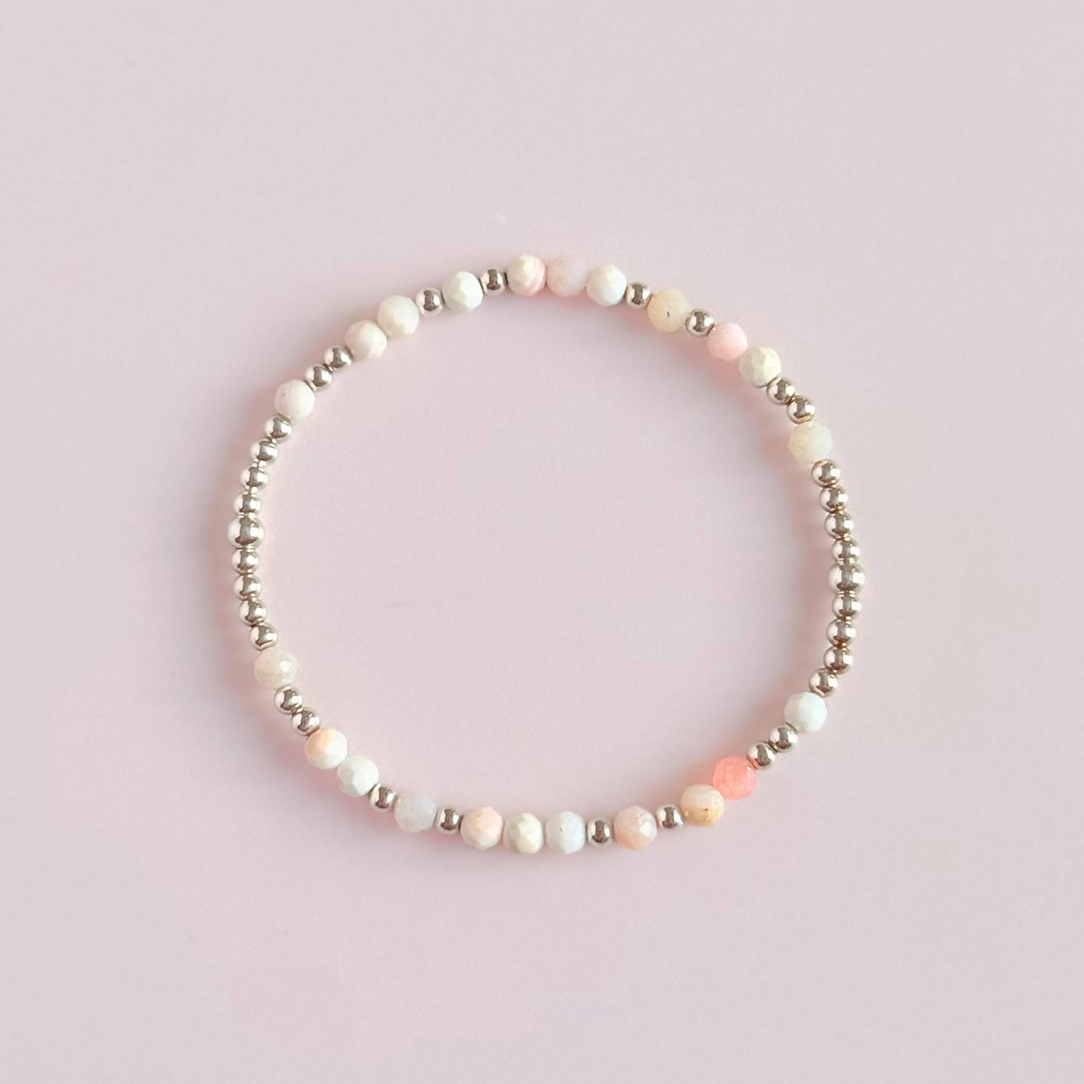 Dainty, minimalist sterling silver and pink opal October birthstone stacking bracelet. Made with 4mm faceted pink opal beads and 3mm sterling silver round beads. Elasticated for comfort. Pictured from above