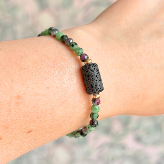 Essential oil diffuser bracelet featuring black lava rock tube bead on the band of 4mm faceted ruby in zoisite beads. Finished with your choice of sterling silver or gold vermeil accent beads.