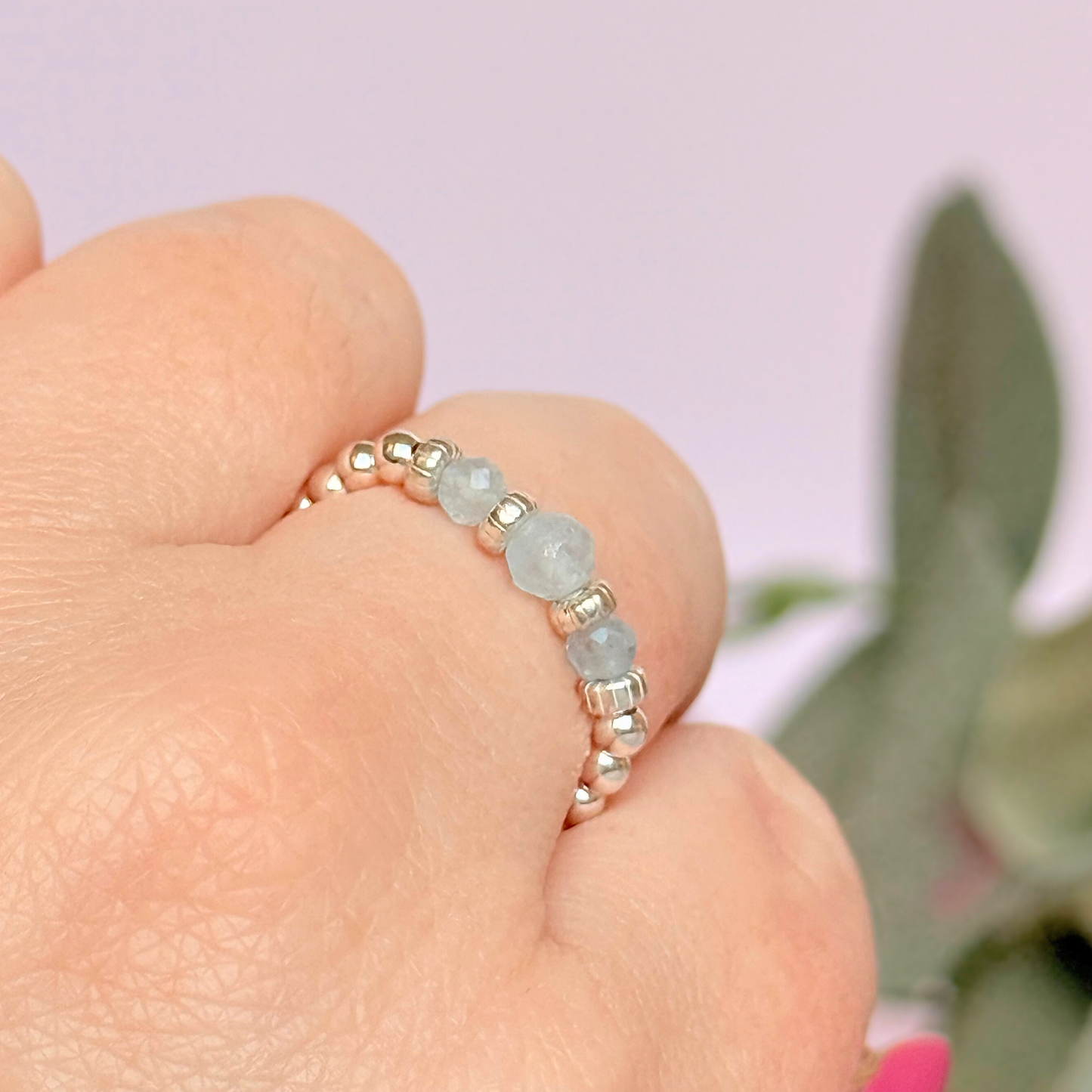Aquamarine crystal trilogy sterling silver elasticated ring featuring three March birthstone gemstone faceted beads, on a band of sterling silver round beads. The crystals are seperated by sterling silver corrugated rondelles. The main crystal is 4mm and the ones at either side are 3mm. Pictured being worn, on an angle.