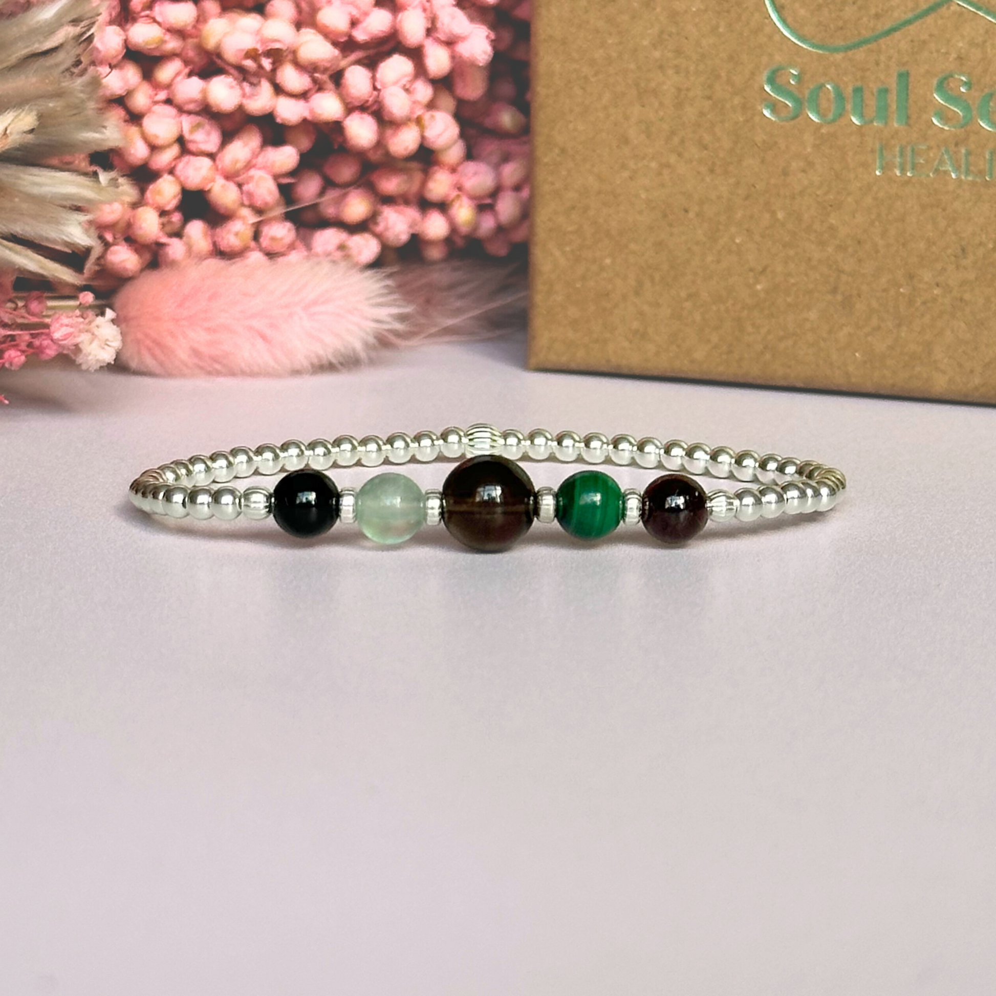 This sterling silver Capricorn bracelet is made with a selection of five healing crystals all believed to resonate with the Capricorn zodiac sign. The central bead is 8mm, the other four are 6mm. On an elasticated band of 3mm sterling silver beads with corrugated accent beads. Featuring garnet, malachite, fluorite, smoky quartz and black tourmaline.