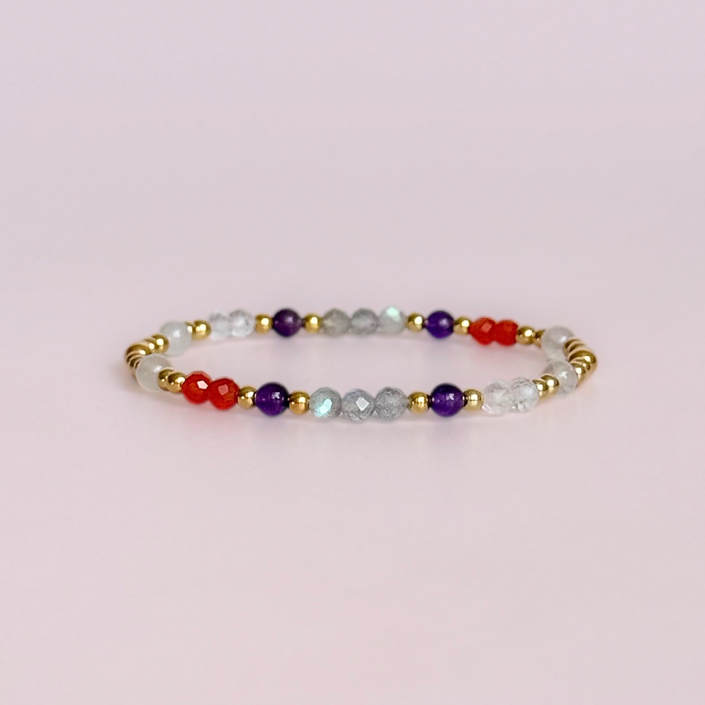 Dainty gold vermeil crystal bracelet featuring five crystals, in 4mm faceted and smooth round style, each believed to help with hormonal balance. Featuring amethyst, moonstone, carnelian, labradorite and rose quartz. Pictured against a pink background.