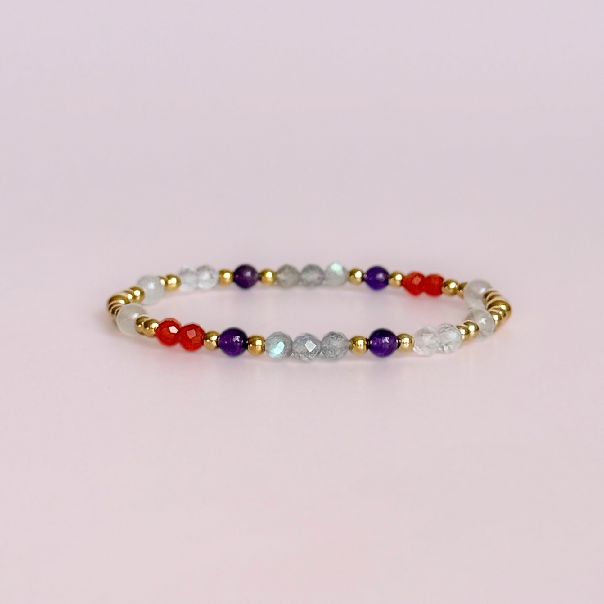 Dainty gold vermeil crystal bracelet featuring five crystals, in 4mm faceted and smooth round style, each believed to help with hormonal balance. Featuring amethyst, moonstone, carnelian, labradorite and rose quartz. Pictured against a pink background.