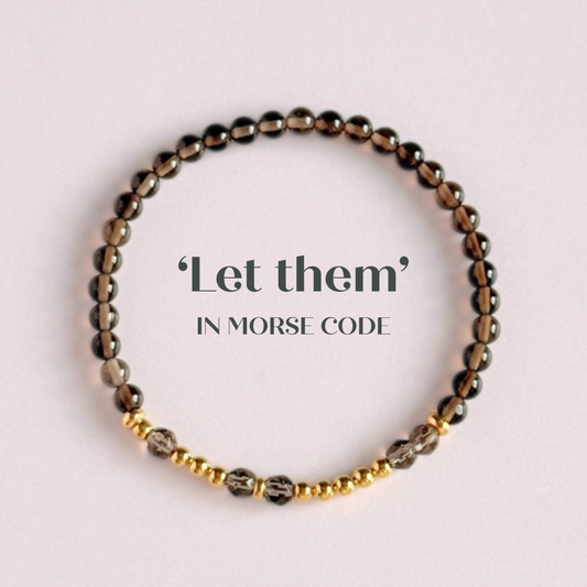 Elasticated smoky quartz crystal morse code bracelet that spells out the words ‘Let them’ in a combination of 4mm round smoky quartz beads, 4mm faceted smoky quartz beads and either sterling silver or gold vermeil 3mm round beads. The words start and end at the rondelle spacer beads.