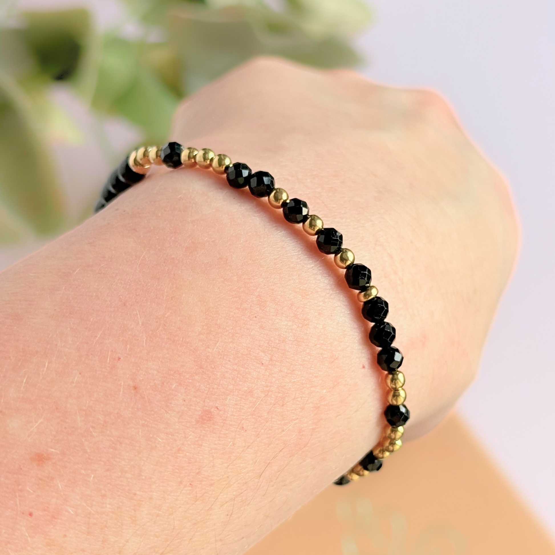 Elasticated black tourmaline crystal morse code bracelet spells out the words ‘Fuck off’ in a combination of 4mm round black tourmaline beads, 4mm faceted black tourmaline beads and either sterling silver or gold vermeil 3mm round beads. The words start and end at the rondelle spacer beads. Picture shows gold variation being worn, shown at an angle