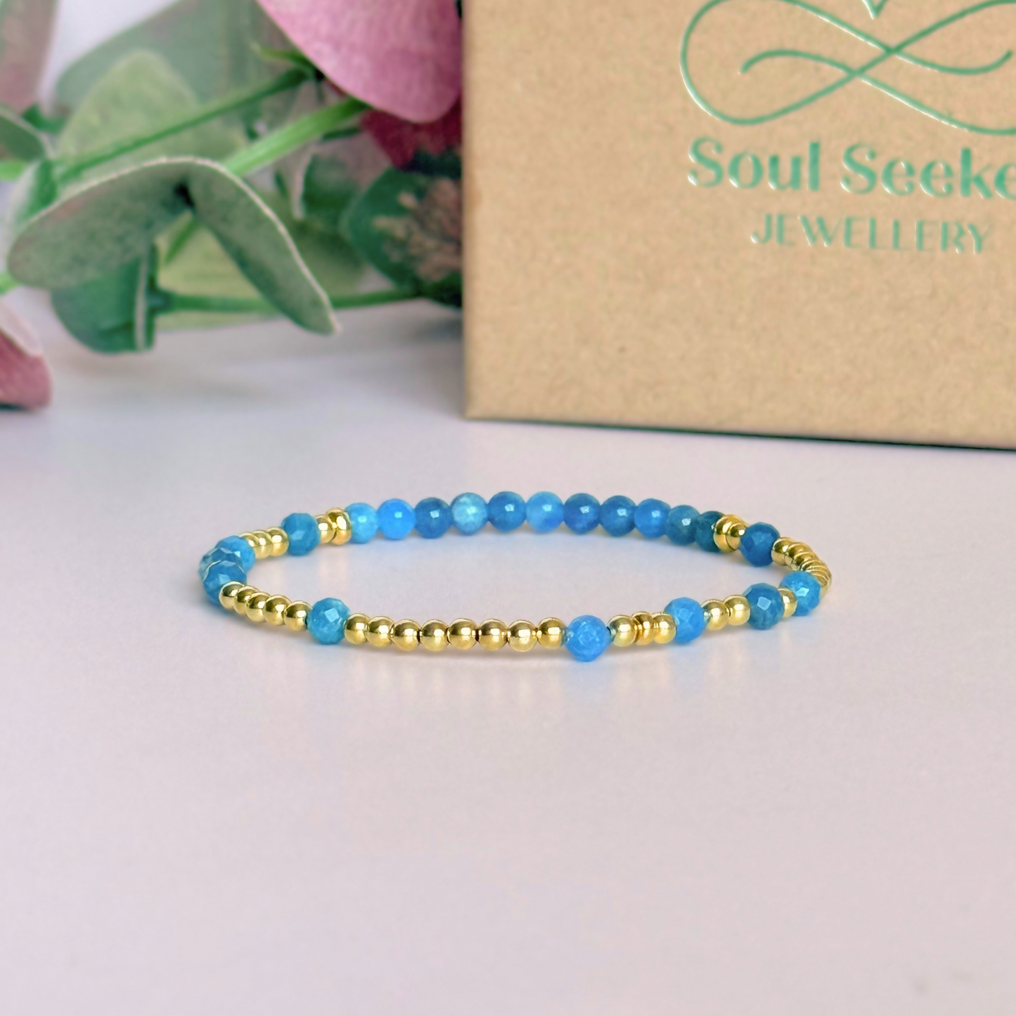 Apatite morse code bracelet that spells out the words ‘Ask, believe, receive’ in a combination of 4mm round smooth and faceted crystal beads with your choice of sterling silver or gold vermeil accent beads. Pictured in gold, in front of the gift box