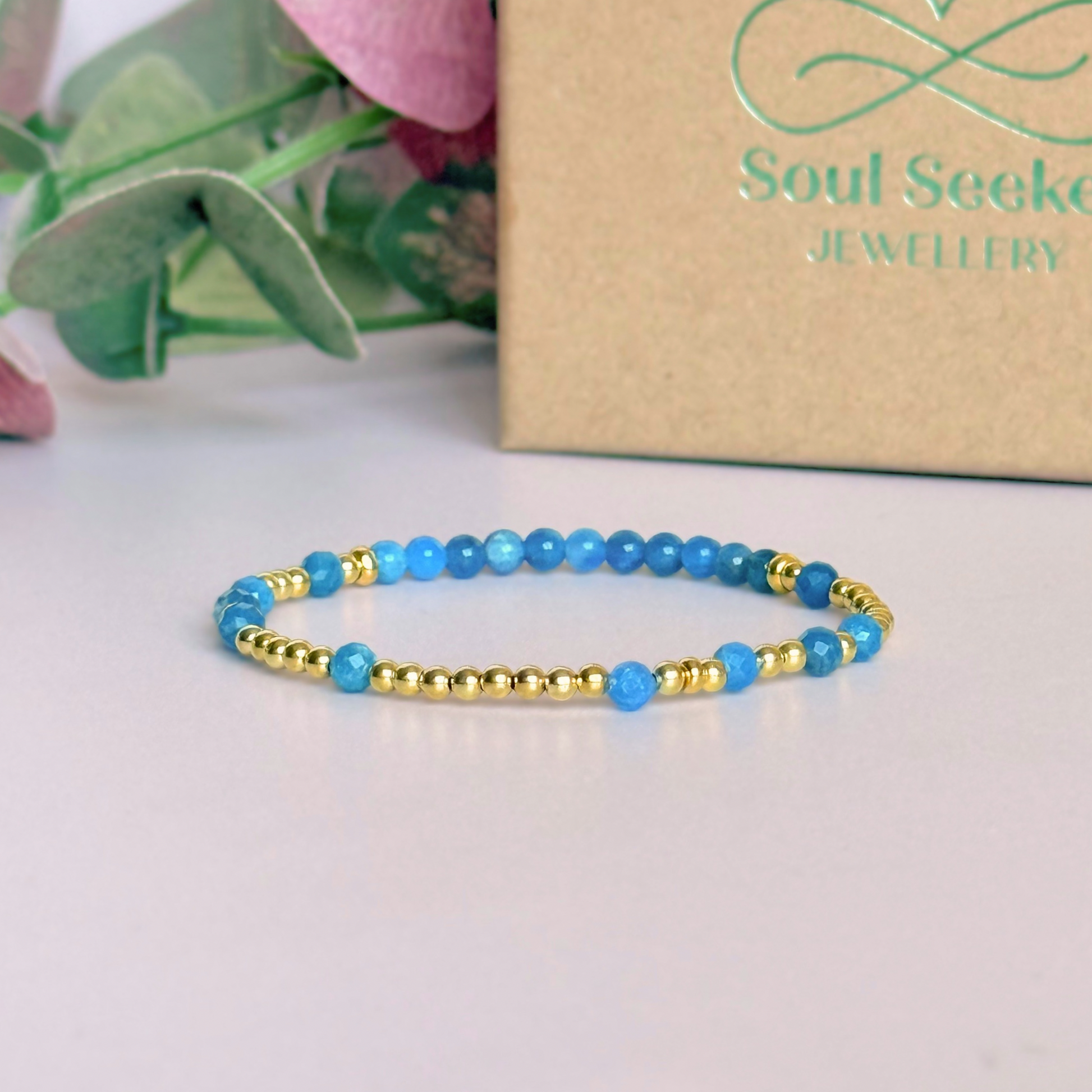 Apatite morse code bracelet that spells out the words ‘Ask, believe, receive’ in a combination of 4mm round smooth and faceted crystal beads with your choice of sterling silver or gold vermeil accent beads. Pictured in gold, in front of the gift box