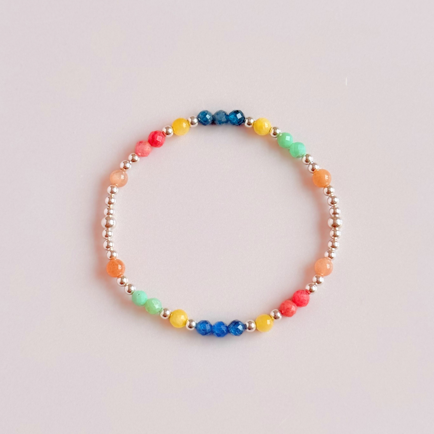 'Key West' sterling silver dainty beaded bracelet with apatite, rhodochrosite, yellow calcite, chrysoprase and peach moonstone. Made with round 3mm sterling silver beads and 4mm smooth and faceted round crystal gemstone beads. Pictured from above, against a pink background