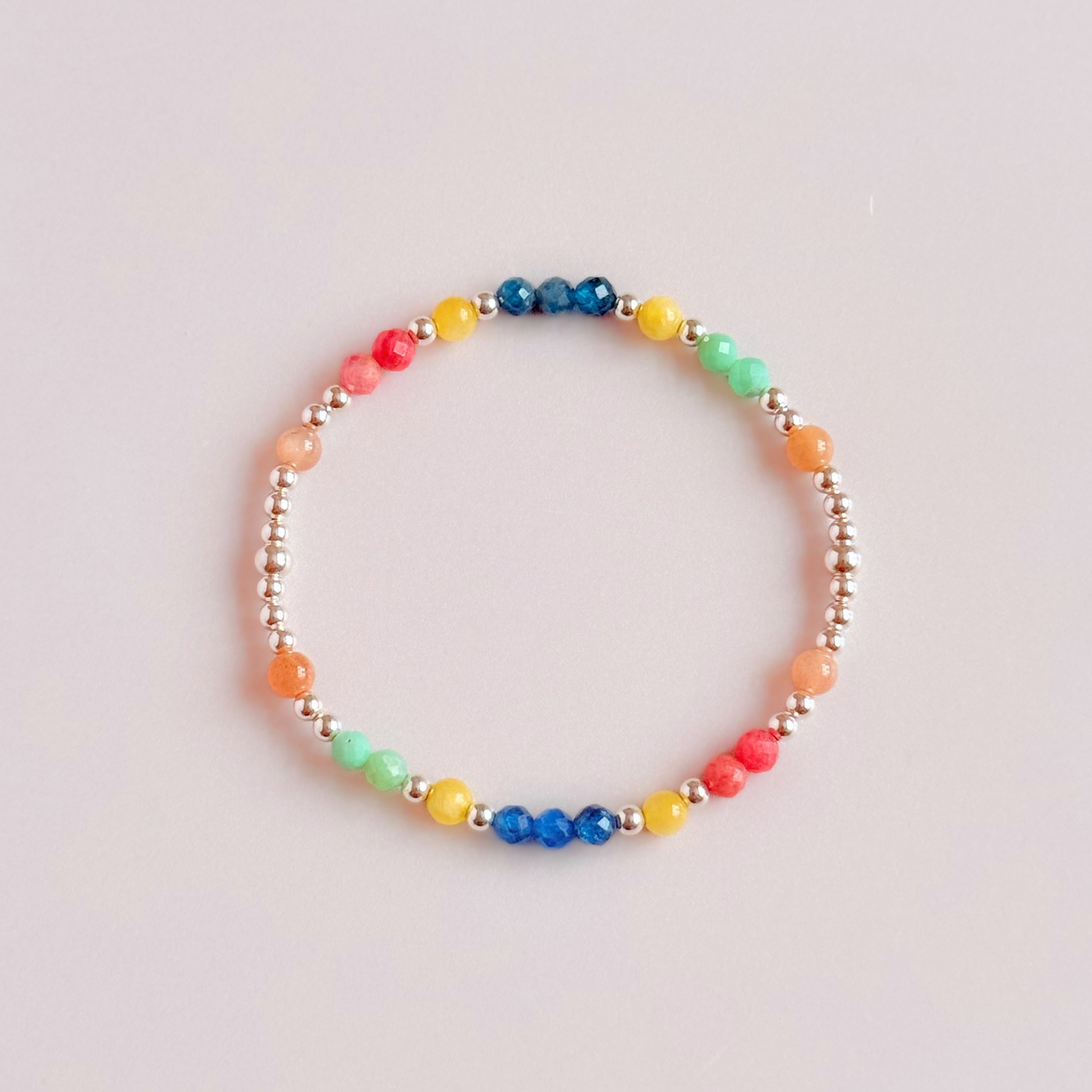 'Key West' sterling silver dainty beaded bracelet with apatite, rhodochrosite, yellow calcite, chrysoprase and peach moonstone. Made with round 3mm sterling silver beads and 4mm smooth and faceted round crystal gemstone beads. Pictured from above, against a pink background
