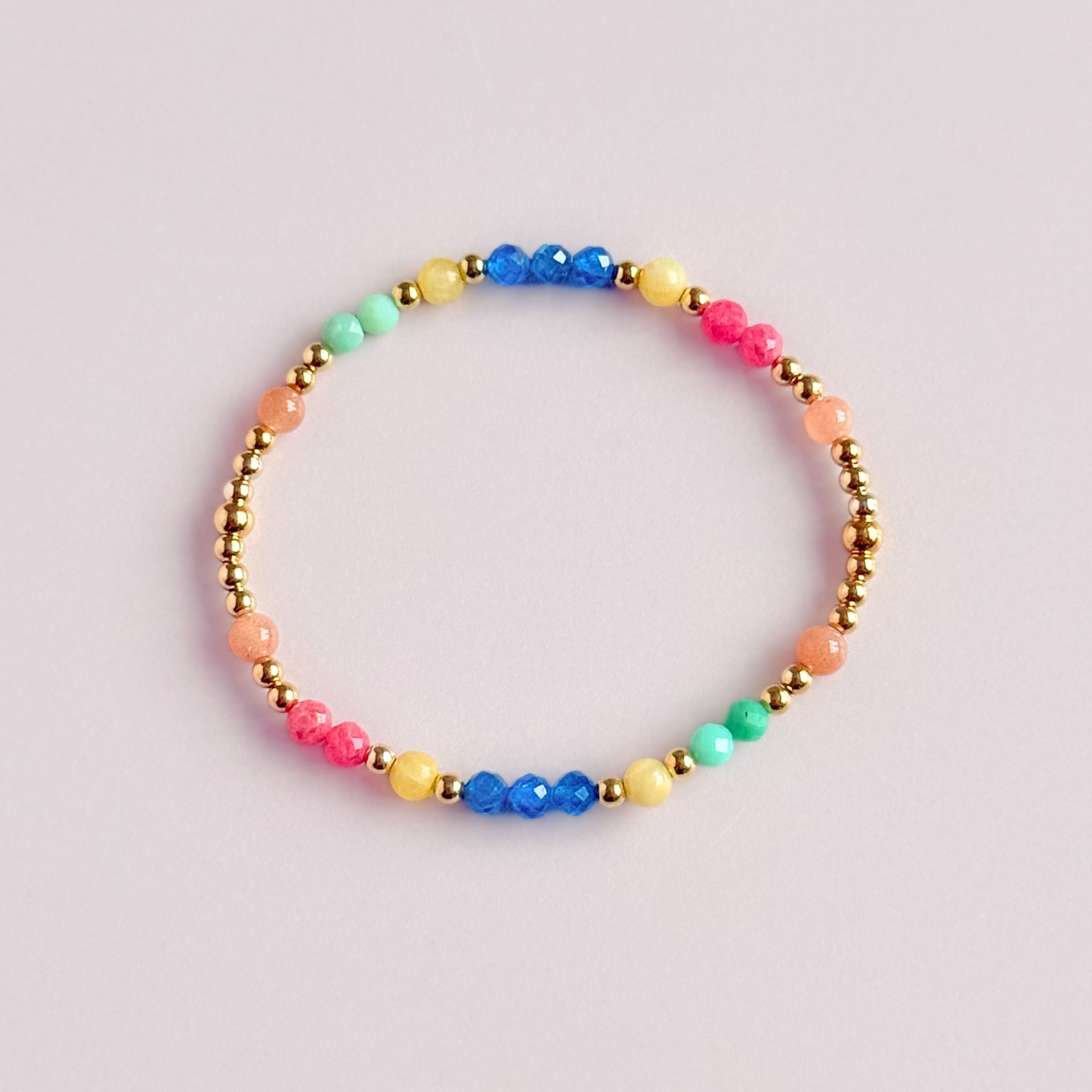 'Key West' gold vermeil dainty beaded bracelet with apatite, rhodochrosite, yellow calcite, chrysoprase and peach moonstone. Made with round 3mm gold vermeil beads and 4mm smooth and faceted round crystal gemstone beads. Pictured from above, against a pink background