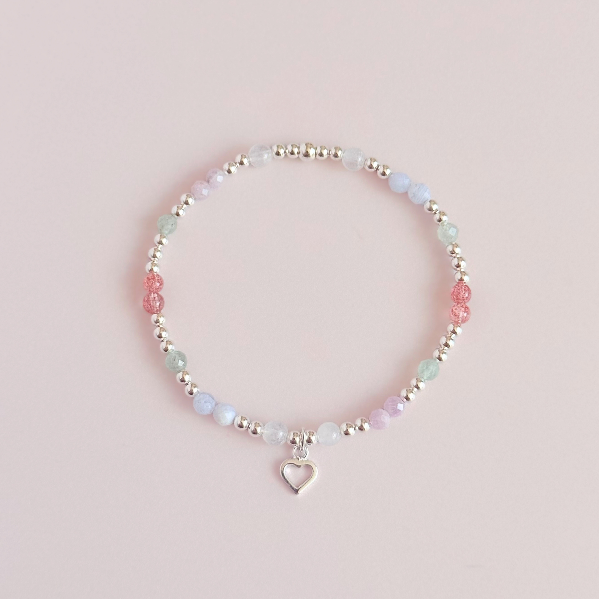 'Soft girl summer' sterling silver dainty beaded bracelet with Kunzite, moonstone, green aventurine, blue lace agate and strawberry quartz . With a beautiful open heart charm.Made with round 3mm sterling silver beads and 4mm smooth and faceted round crystal gemstone beads. Pictured from above, against a pink background