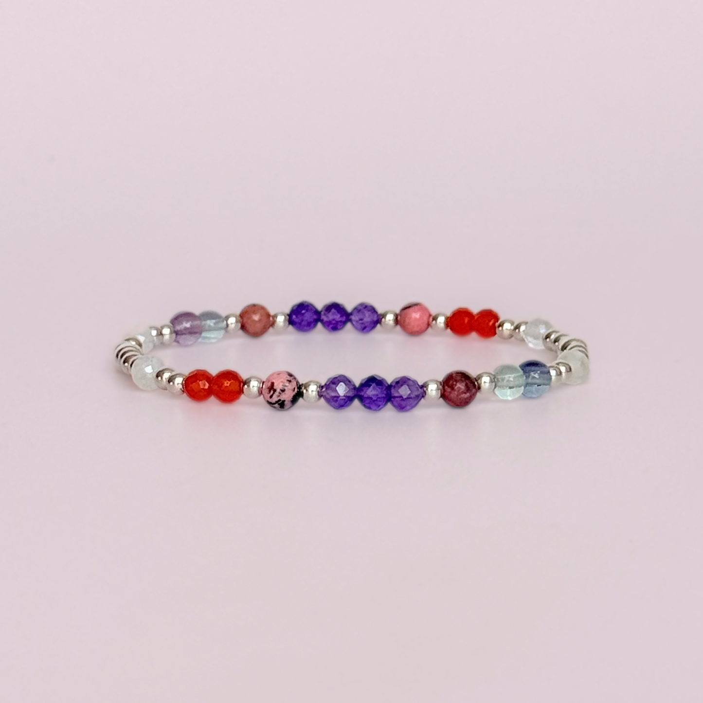 Dainty sterling silver crystal bracelet featuring five crystals, in 4mm faceted and smooth round style, each believed to help with perimenopause symptoms. Featuring amethyst, rhodonite, fluorite, moonstone and carnelian. Pictured against a pink background.