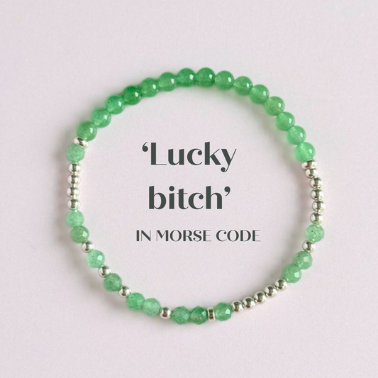 Elasticated green aventurine crystal morse code bracelet spells out the words ‘Lucky bitch’ in a combination of 4mm round green aventurine beads, 4mm faceted green aventurine beads and either sterling silver or gold vermeil 3mm round beads. The words start and end at the rondelle spacer beads.