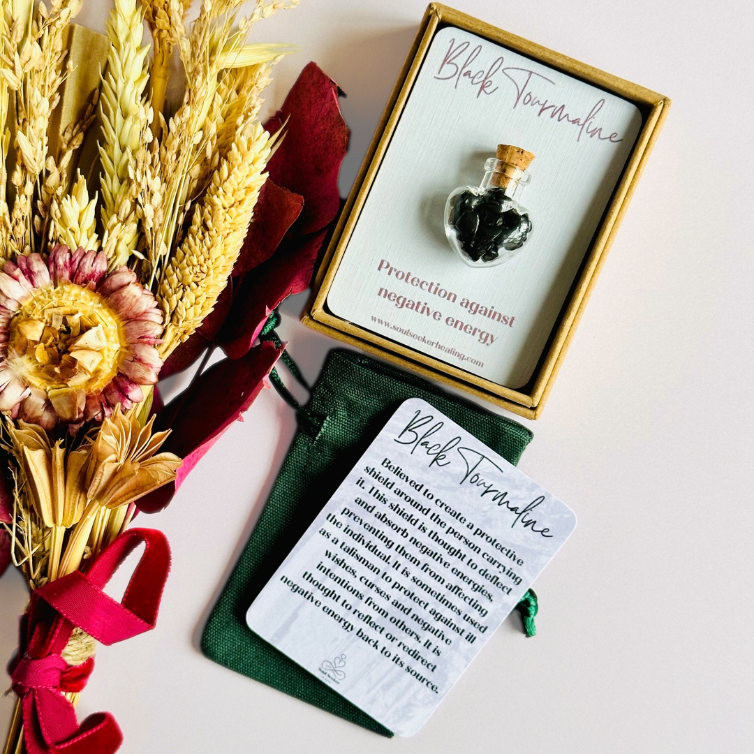 A pretty heart shaped mini glass bottle filled with powerful, ethically mined black tourmaline crystal chips, presented on an eco-friendly textured card with the words 'Protection against negative energy.’