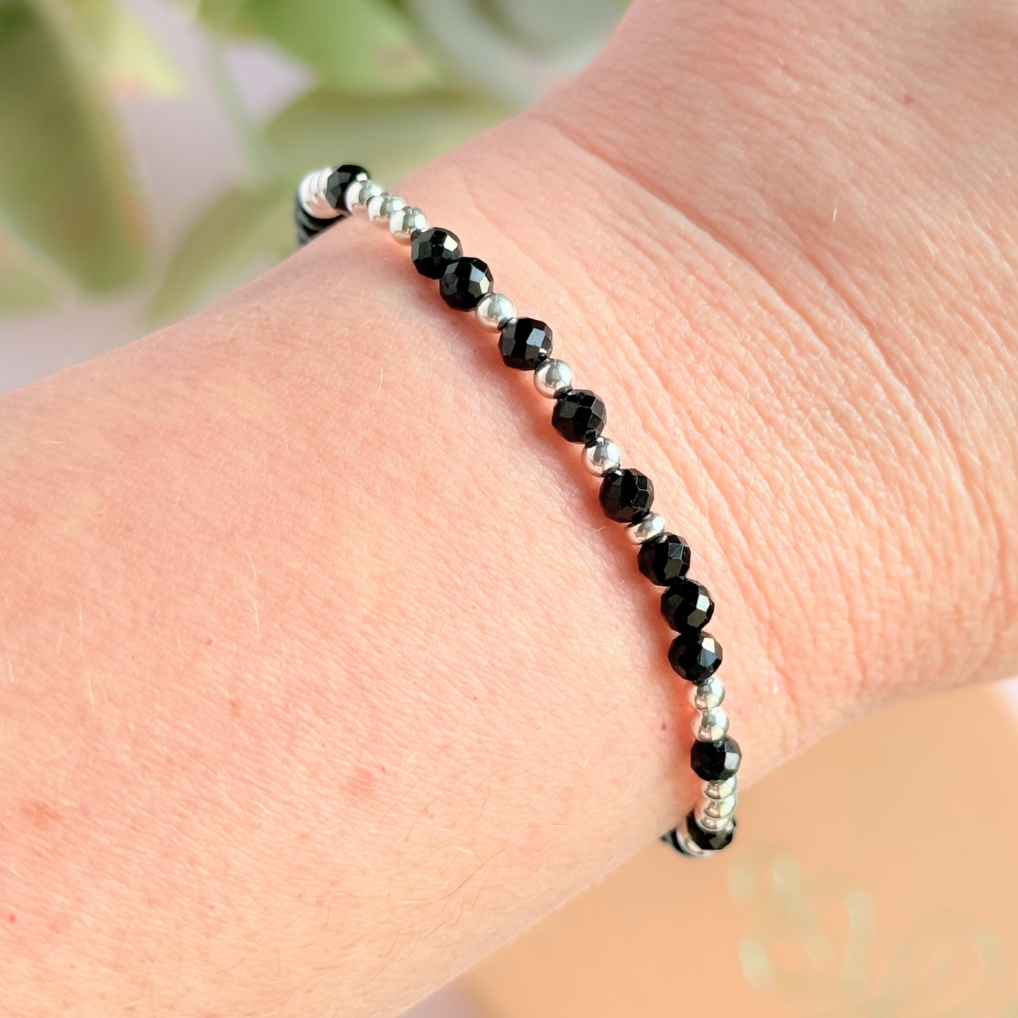 Elasticated black tourmaline crystal morse code bracelet spells out the words ‘Fuck off’ in a combination of 4mm round black tourmaline beads, 4mm faceted black tourmaline beads and either sterling silver or gold vermeil 3mm round beads. The words start and end at the rondelle spacer beads. Picture shows silver bracelet being worn.